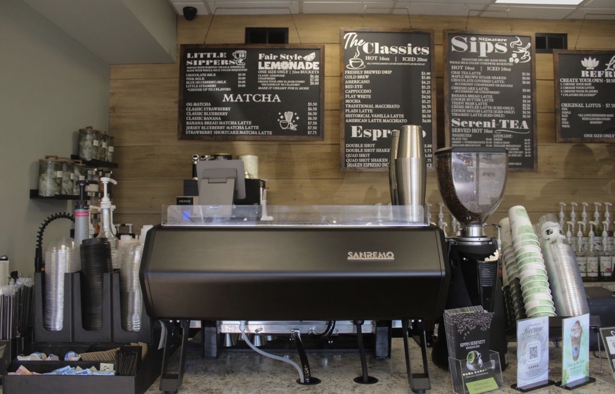 Coffee machine with menu boards above, cups, and supplies on counter in a cafe setting.