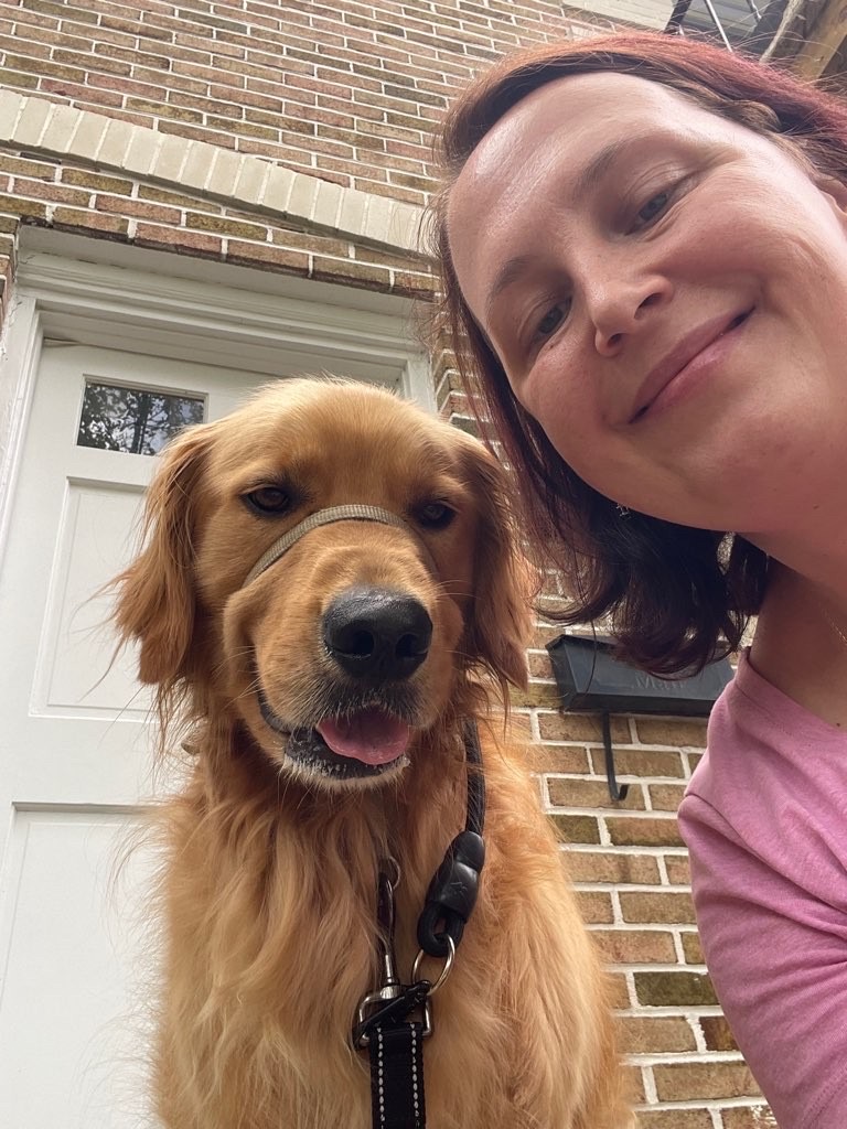 Woman smiling next to a golden retriever outside a brick house, close-up shot.