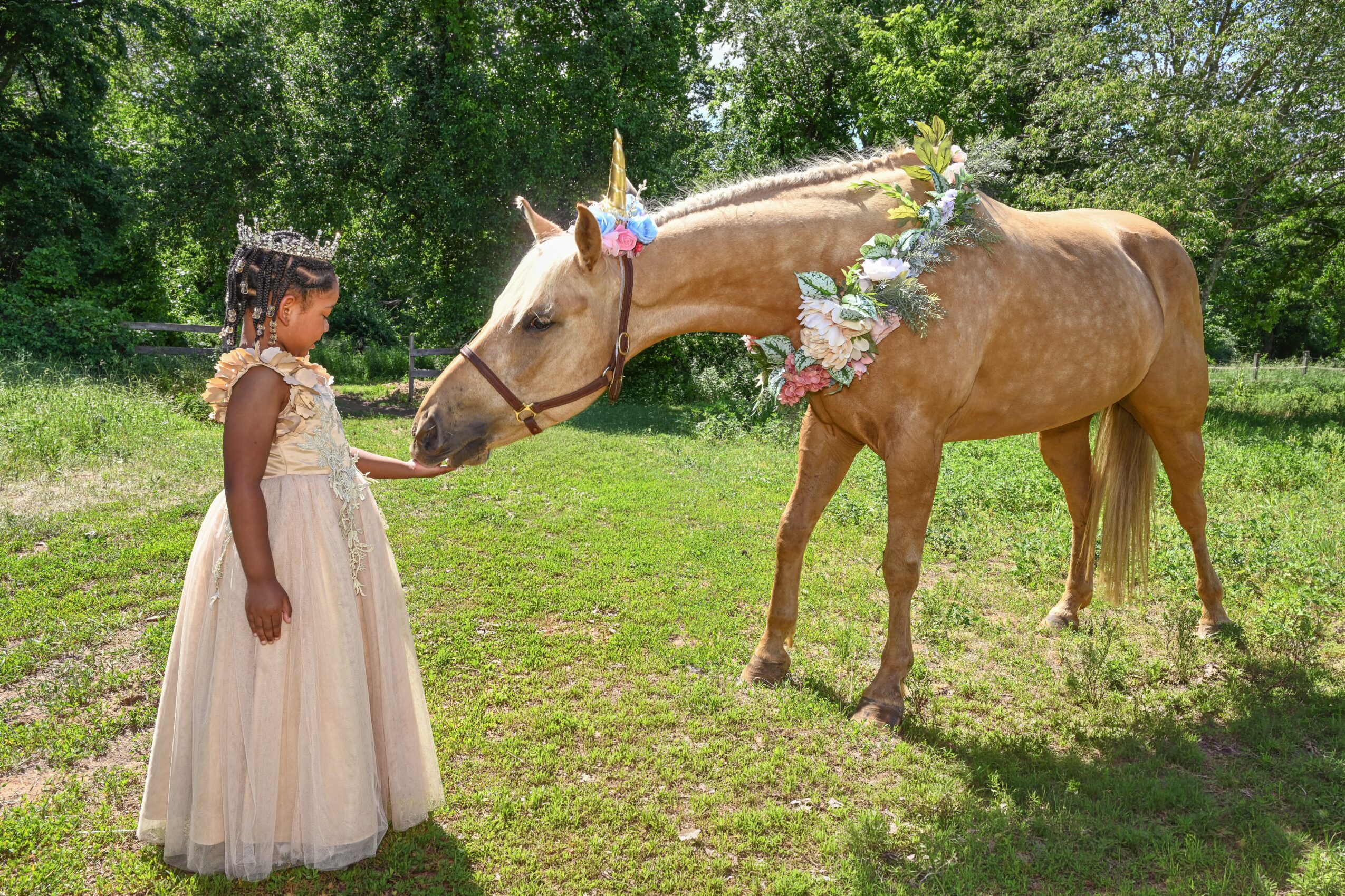 Girl in a dress touching a decorated unicorn in a grassy outdoor setting.