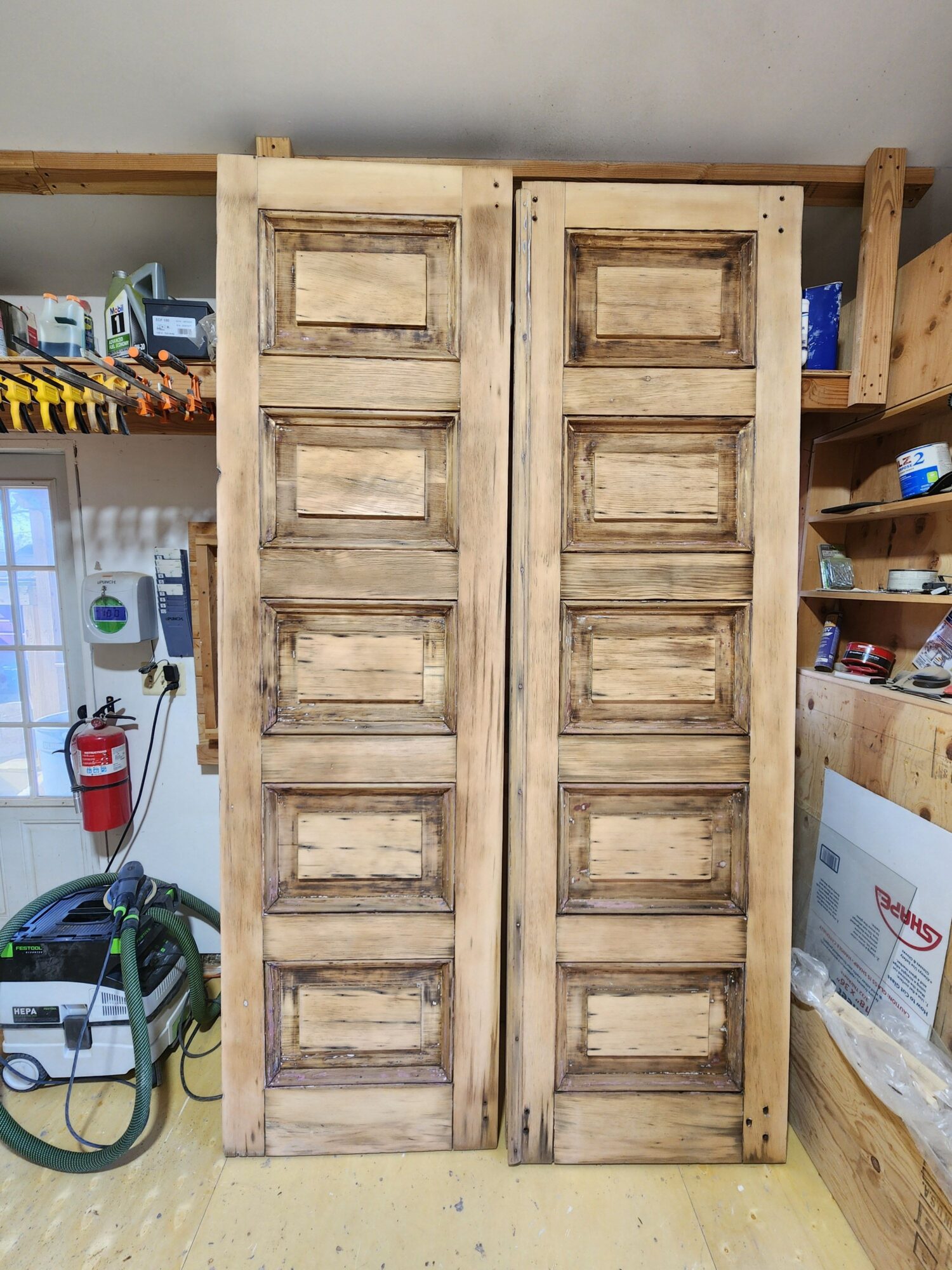Two wooden doors with rectangular panels, leaning against a wall in a workshop or storage area.