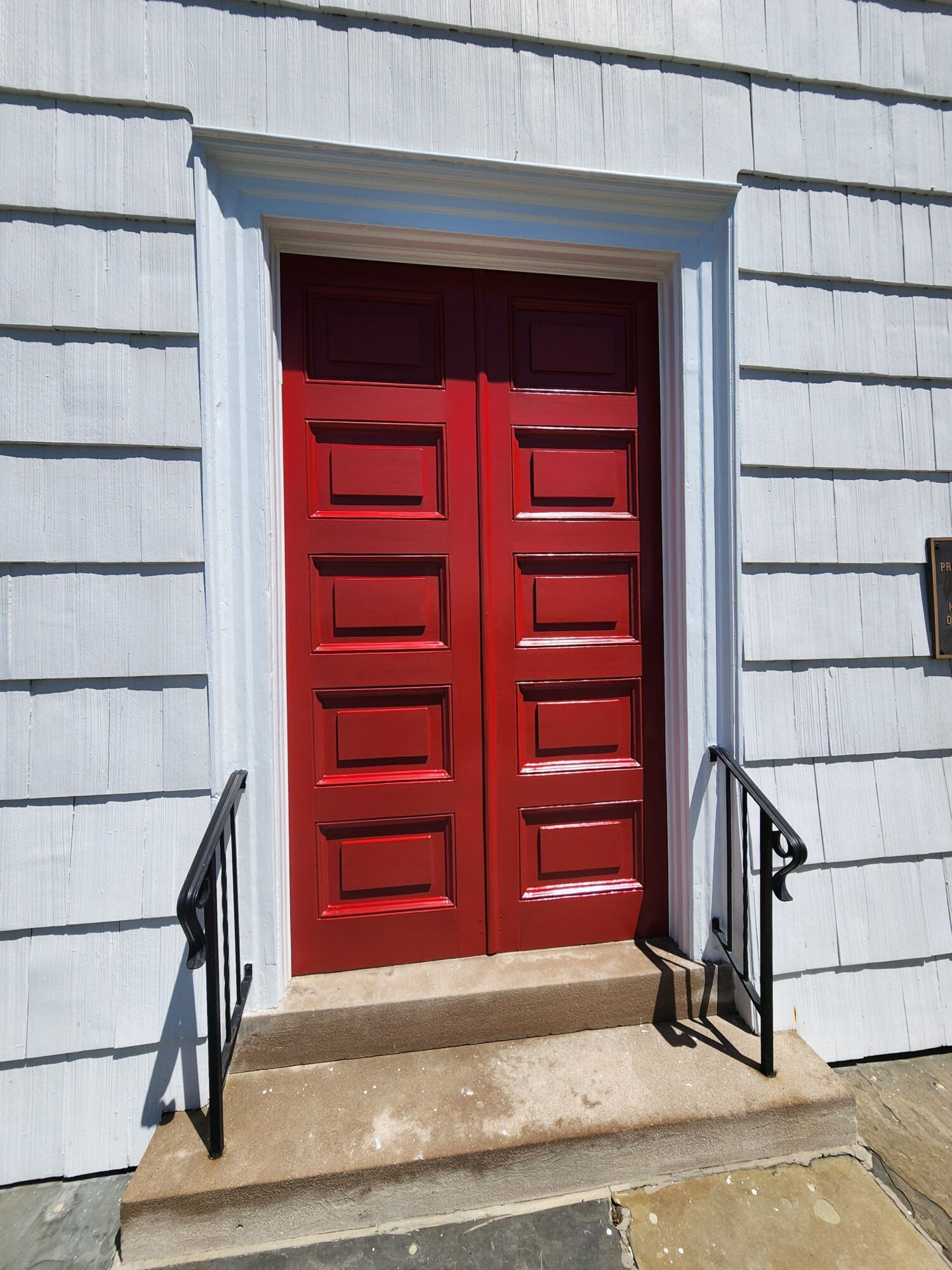 Red garage door with white framing, metal railing on concrete steps, and a light blue building exterior.
