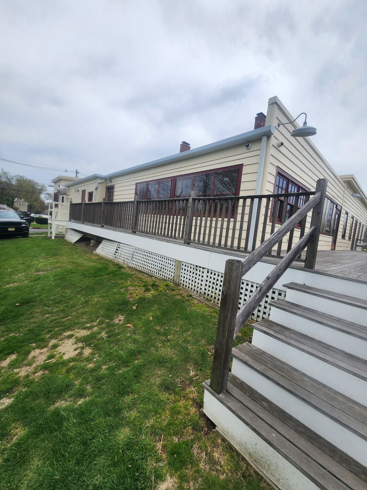 Deck with stairs leading to a house, grass and dirt ground, cloudy sky, and part of the house's exterior visible.