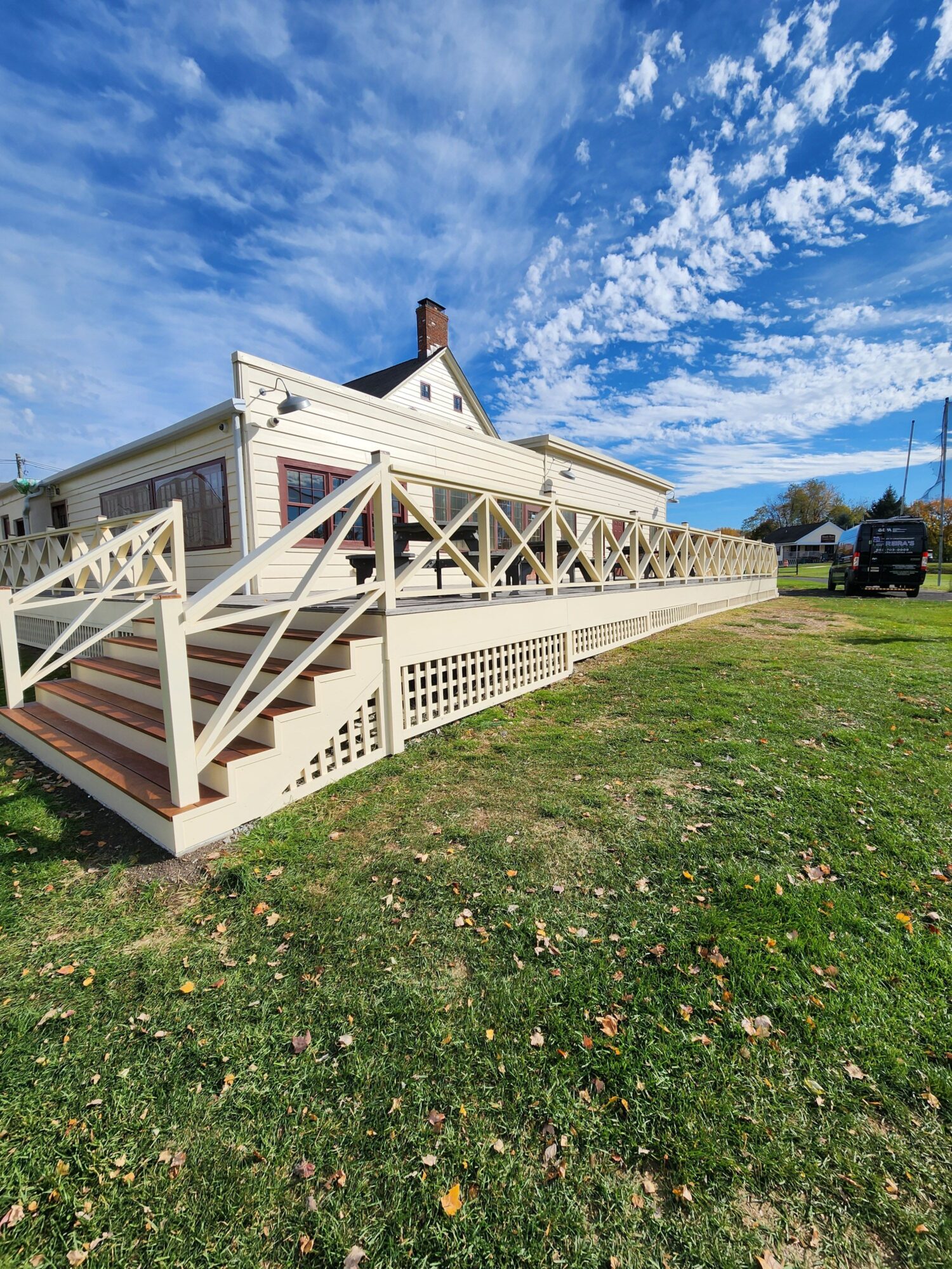 House with a porch, stairs, and railing, on a grassy area under a blue sky with clouds.