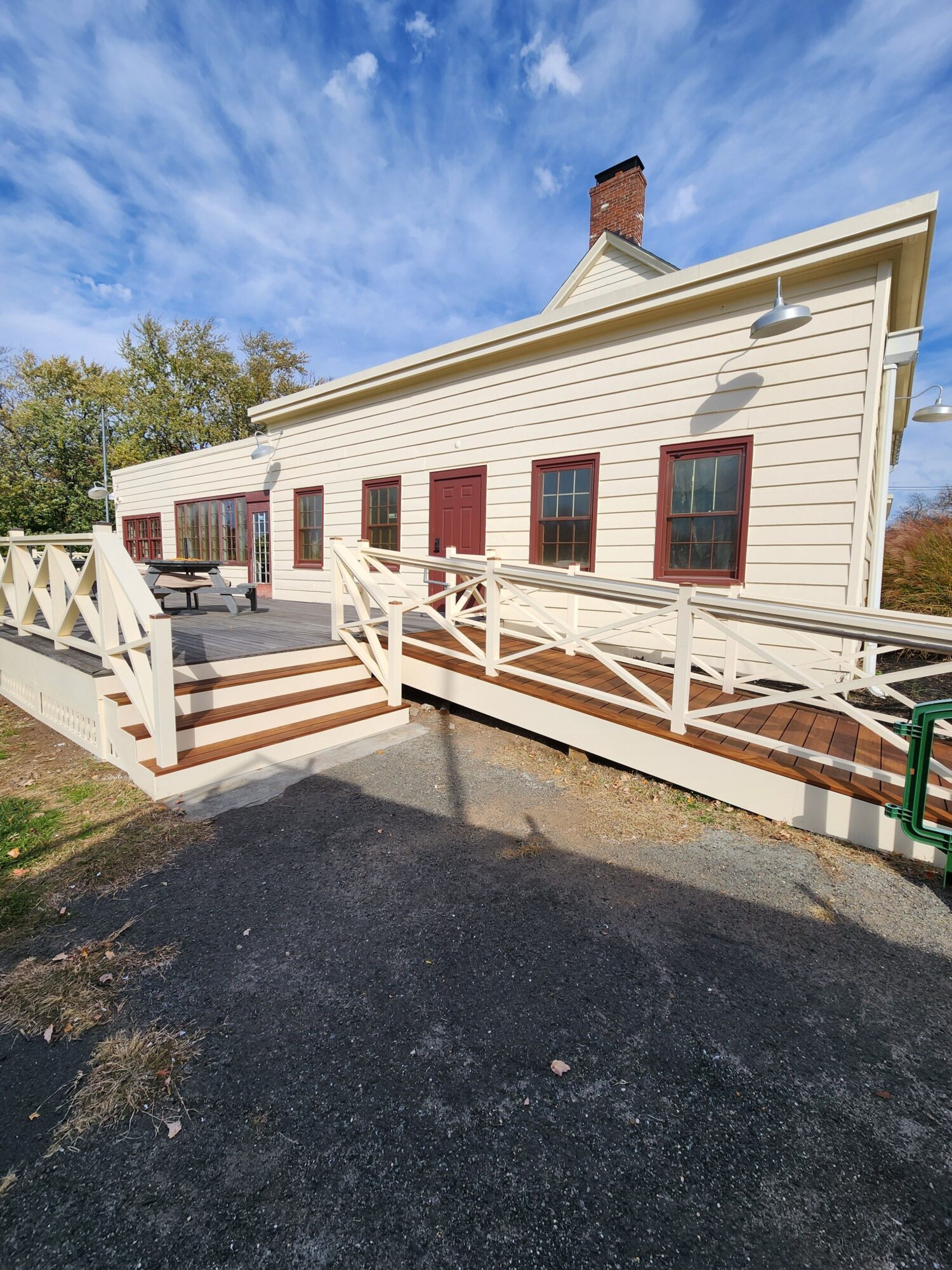 Two-story house with white siding, red window frames, and a small porch, viewed from the side with a wooden ramp.