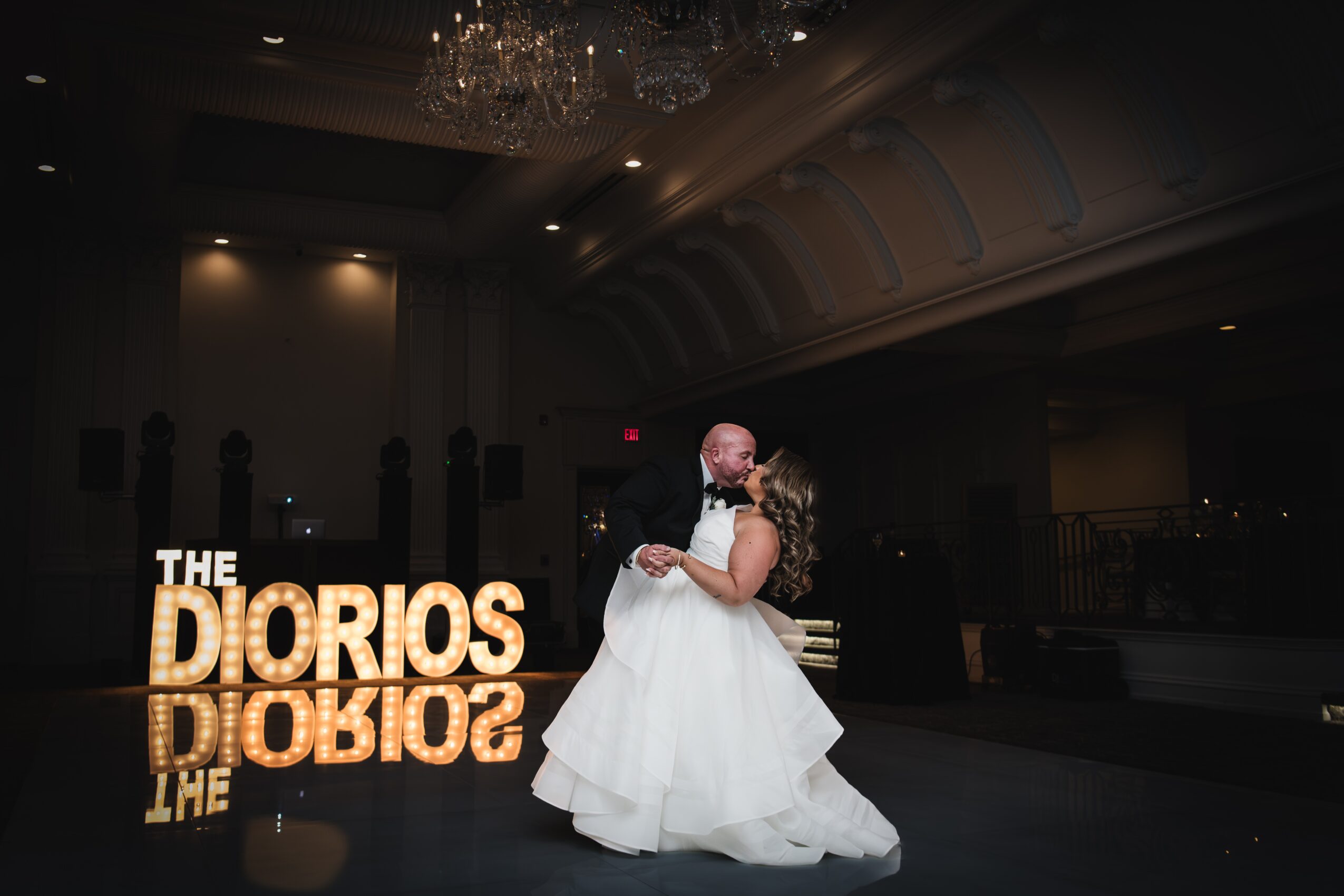 A couple dances in a ballroom with a large illuminated sign reading 'THE DIORIOS' in the background.
