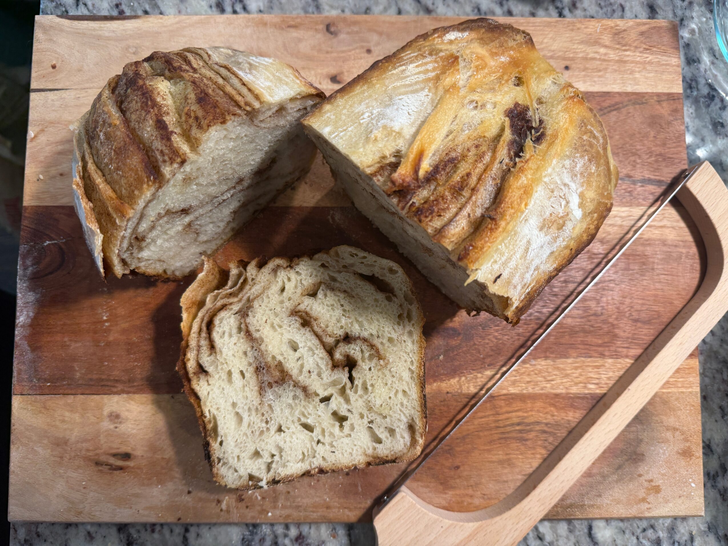Three slices of bread on a wooden cutting board, with a metal bread knife nearby.