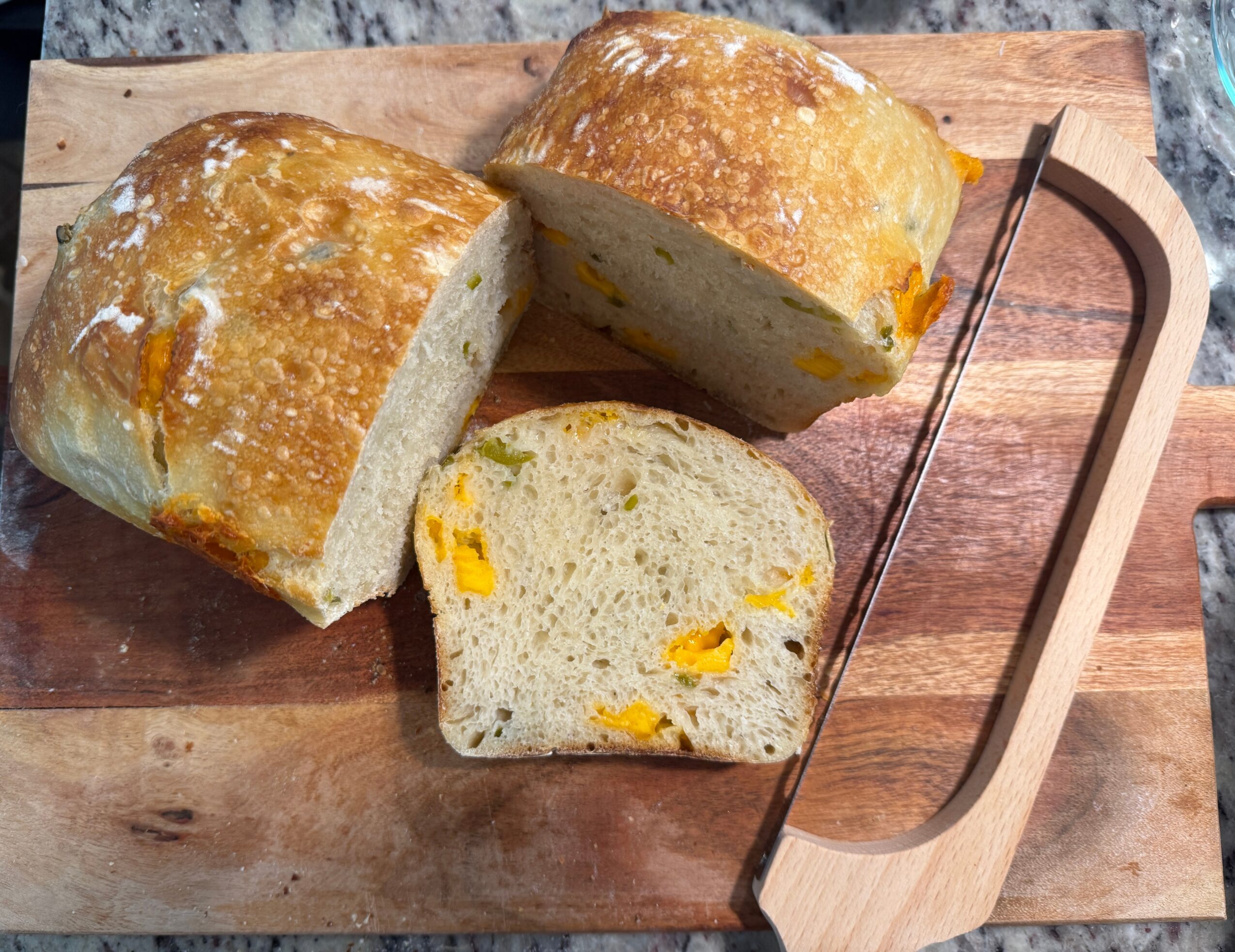 Two bread rolls and a slice of bread with yellow filling on a wooden cutting board, with a metal knife nearby.