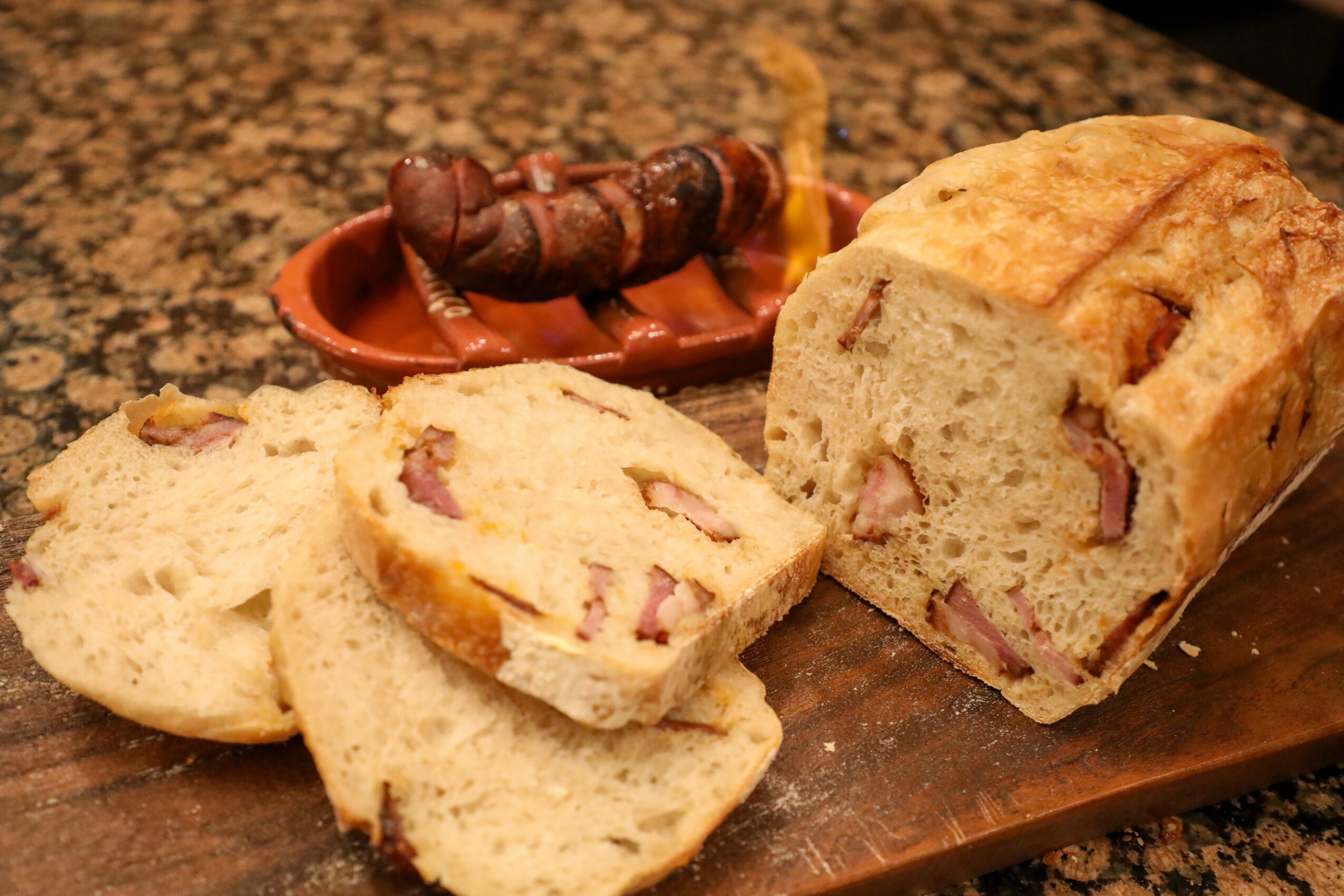 Slices of bread with ham and a roasted insect on a plate in the background, on a wooden surface.
