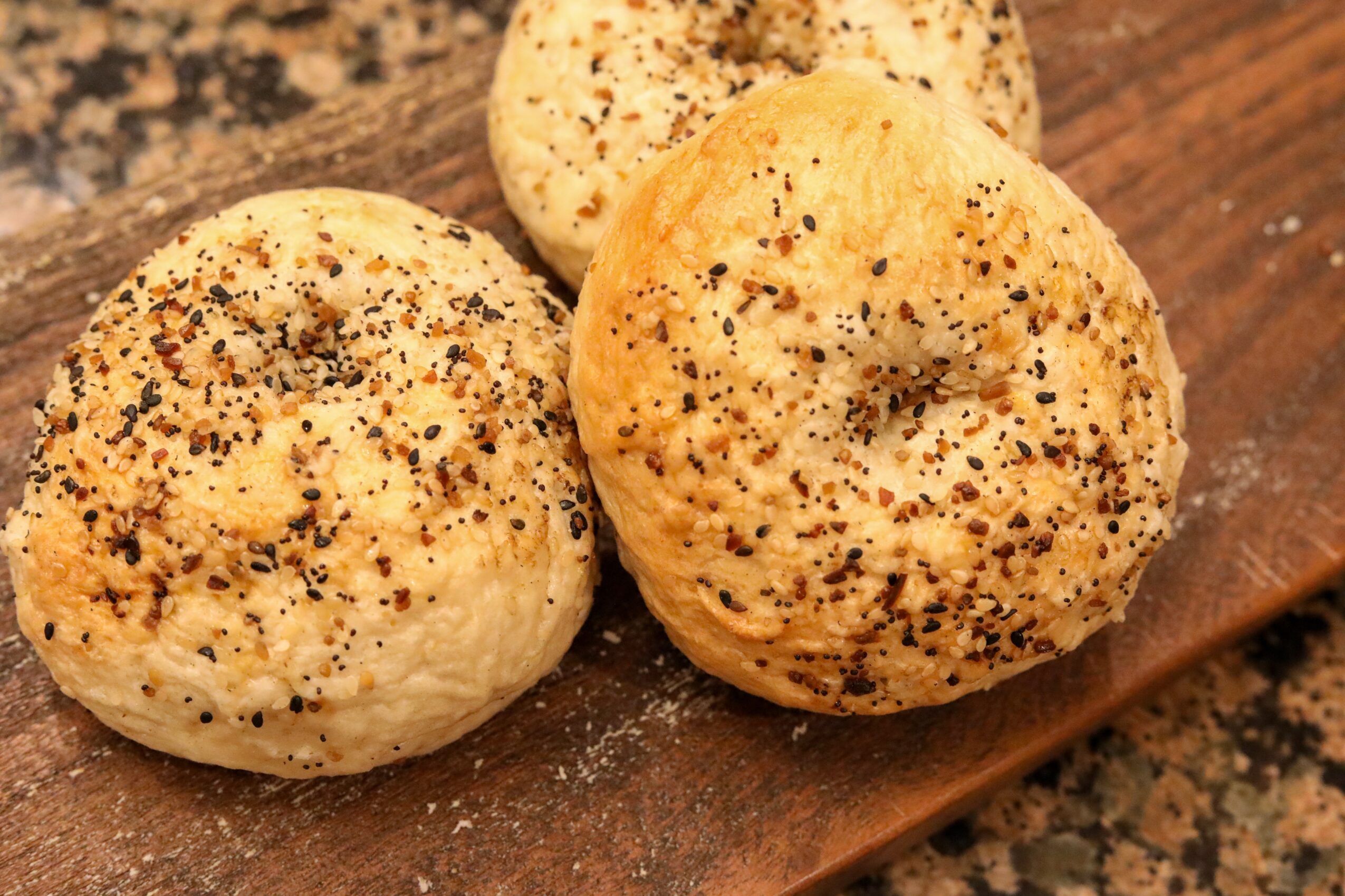Three seasoned bread rolls on a wooden surface, sprinkled with black pepper and herbs.