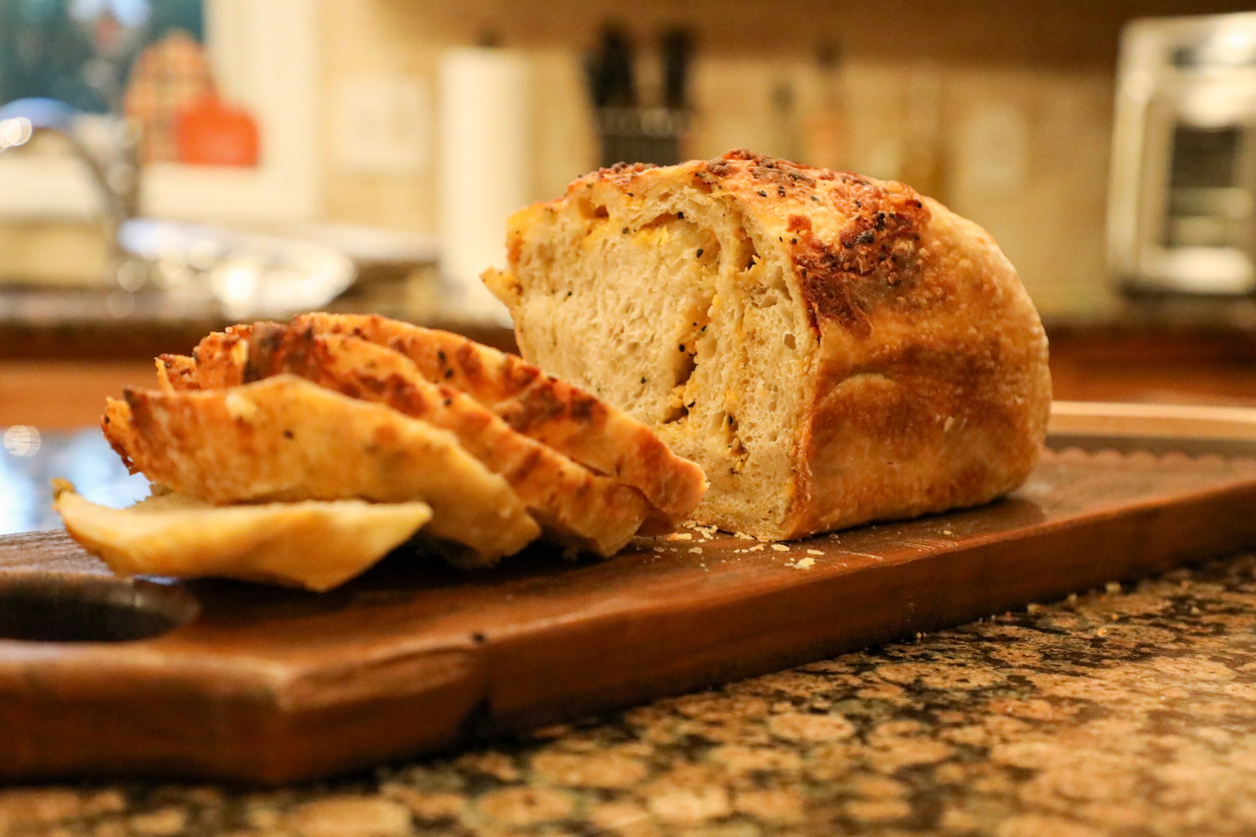 Sliced bread and fried food on a wooden board in a kitchen, with a blurred background.