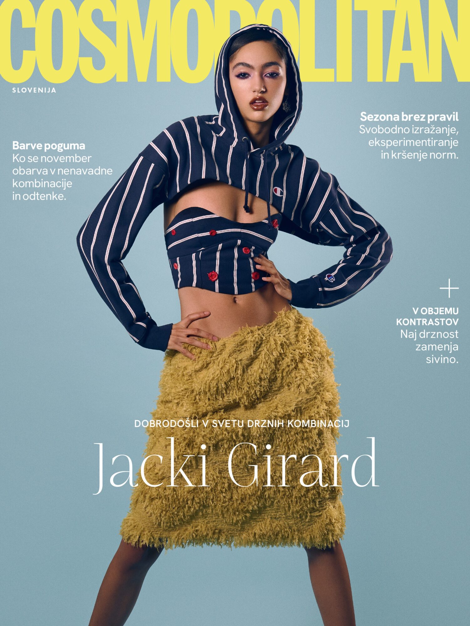 Model with dark hair and makeup wearing a striped jacket and yellow fuzzy skirt, posing against a light blue background.