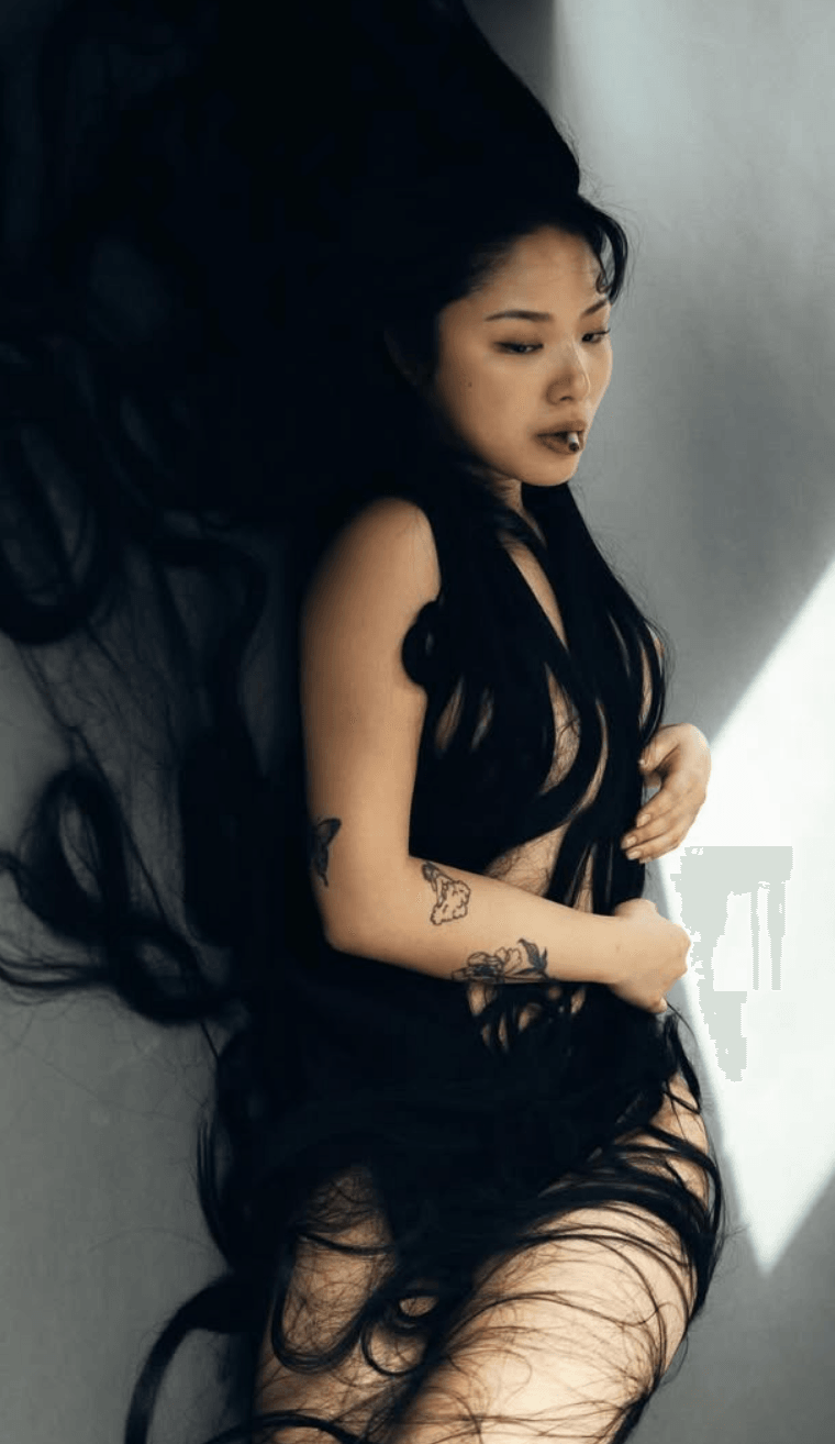 Woman with long dark hair lying on the floor, wearing black clothing, with shadows and light on her face and body.