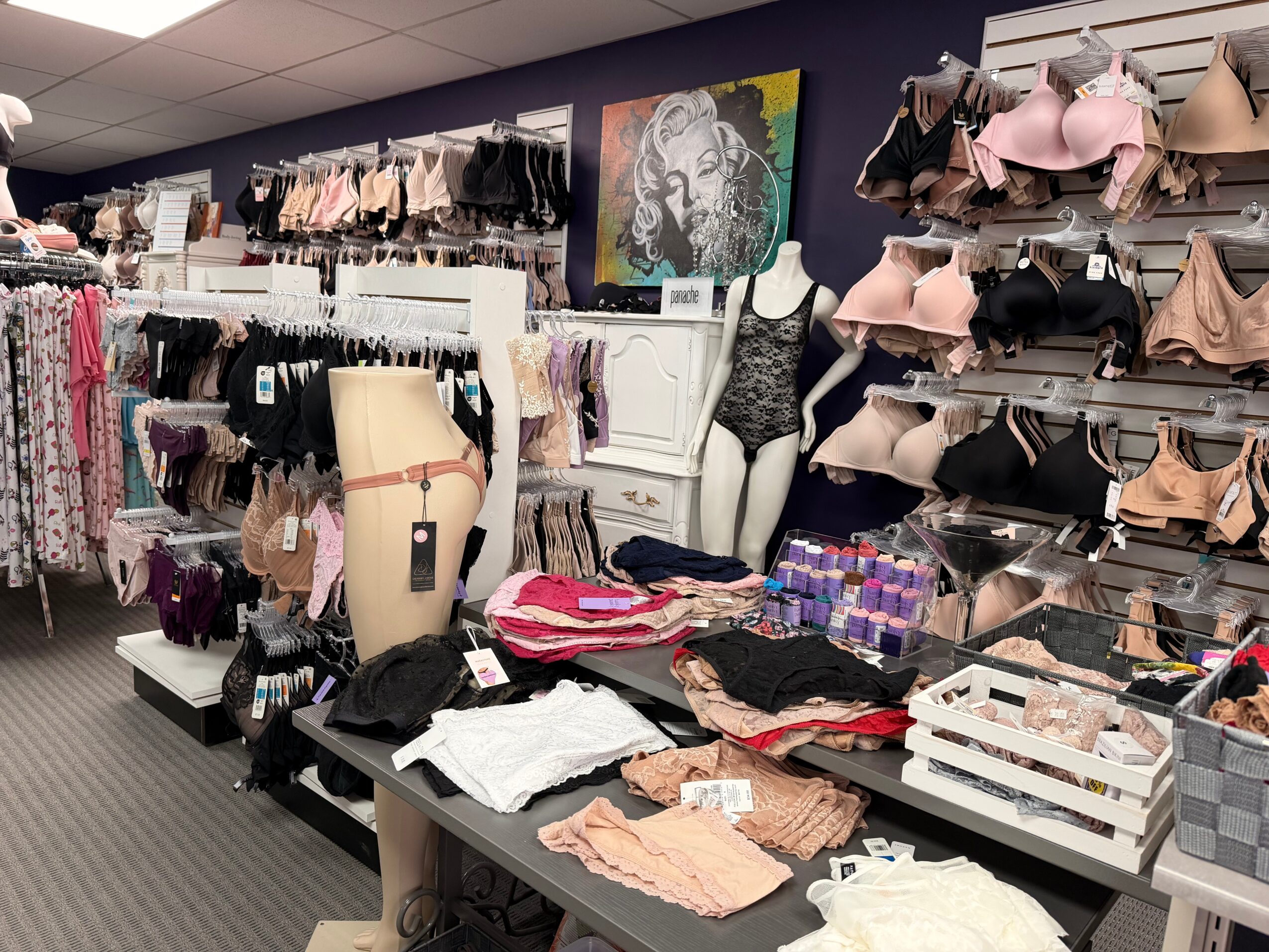 Lingerie and clothing displayed on mannequins and shelves in a store, with a Marilyn Monroe artwork on the wall.