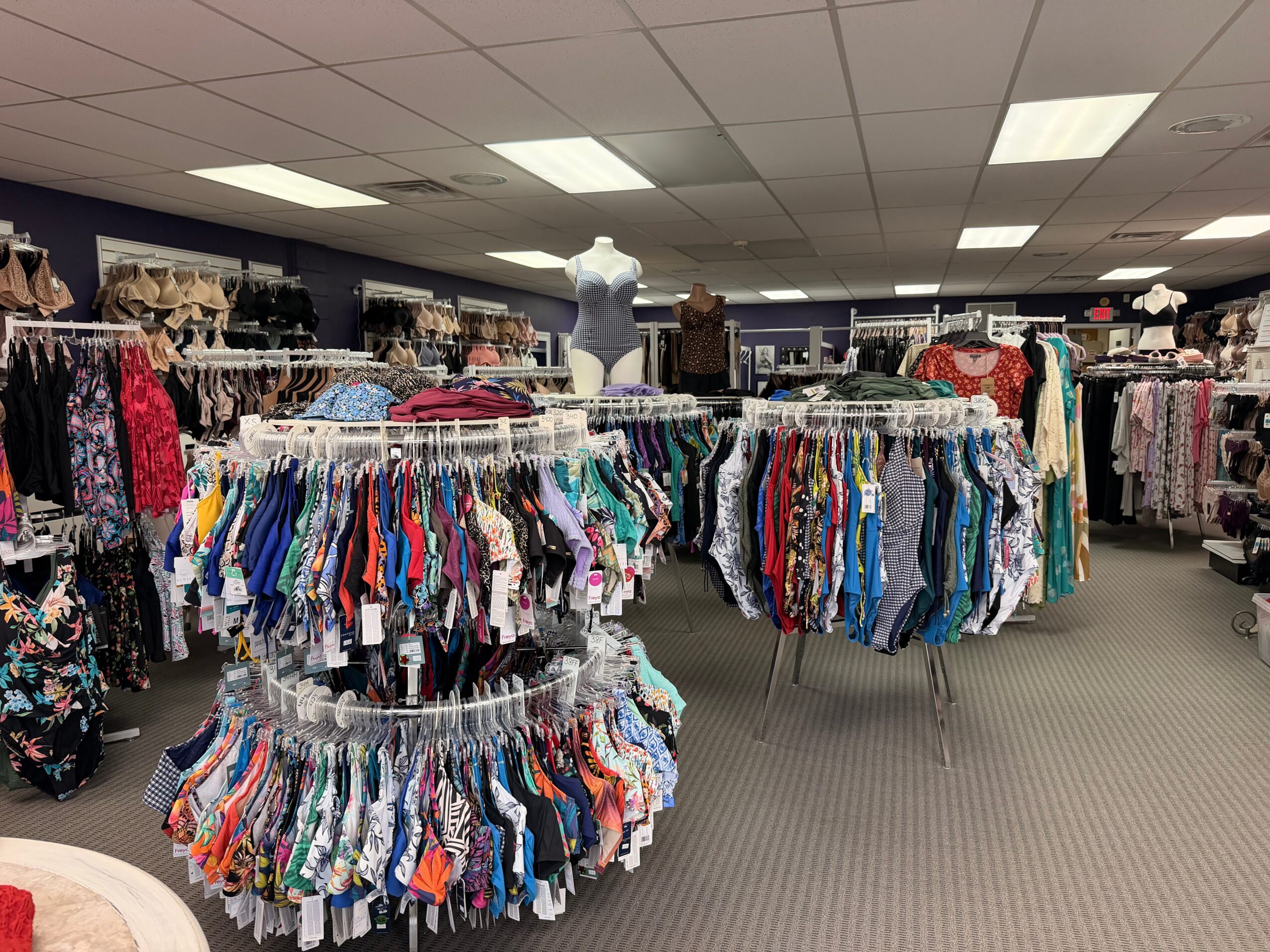 Clothing racks with colorful garments in a store, ceiling lights, and shelves in the background.