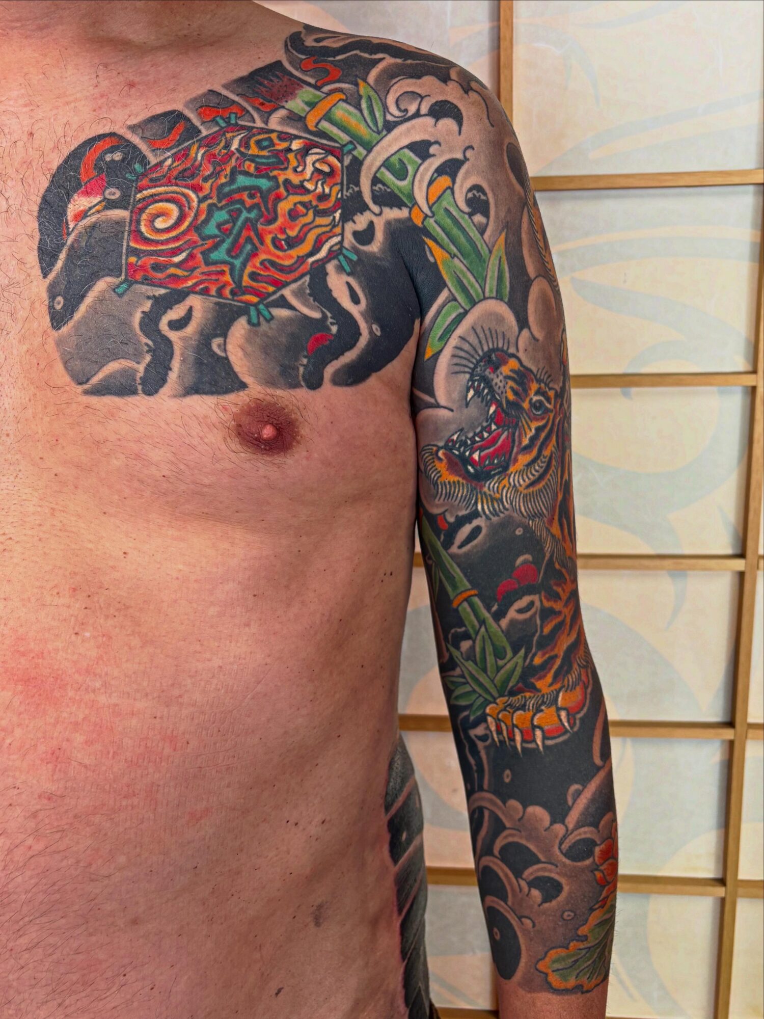 Tattoo of a colorful dragon on person's chest and arm, with clouds and traditional Japanese design elements.