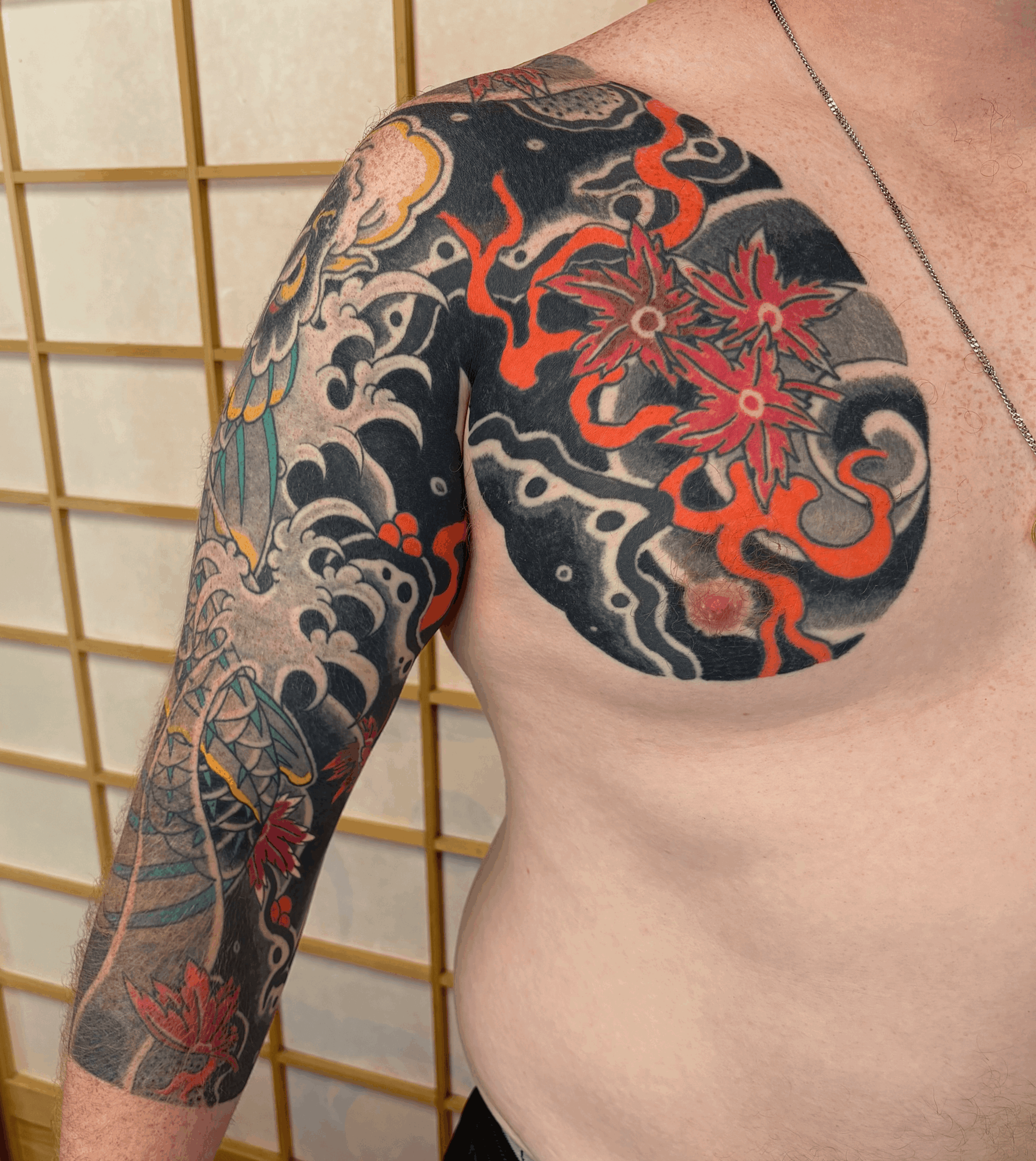 Partially visible person's upper body with colorful tattoo sleeve on arm and shoulder, background of wooden grid panel.