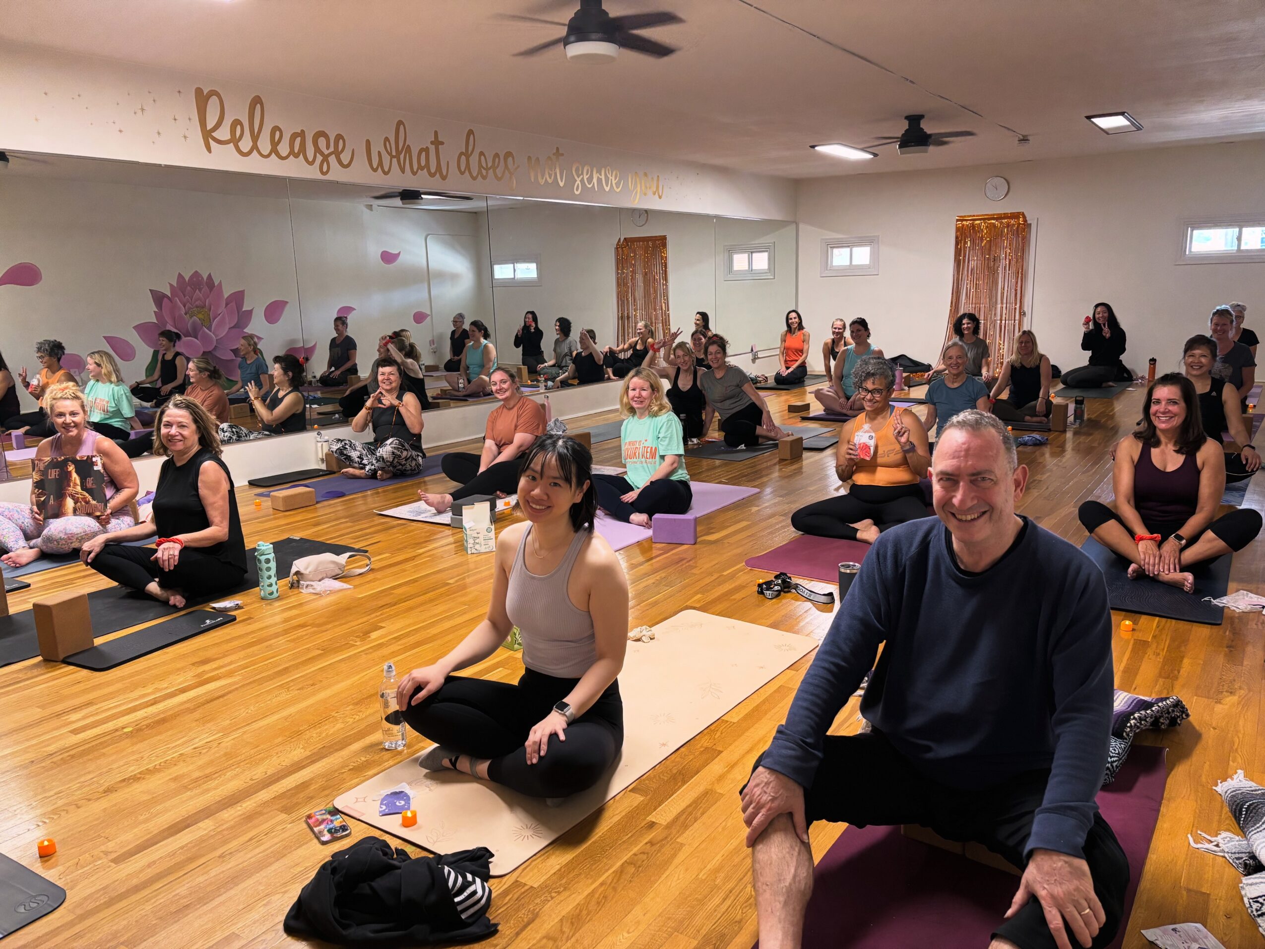 Group of people participating in a yoga class in a spacious room with wooden floors and wall decorations.