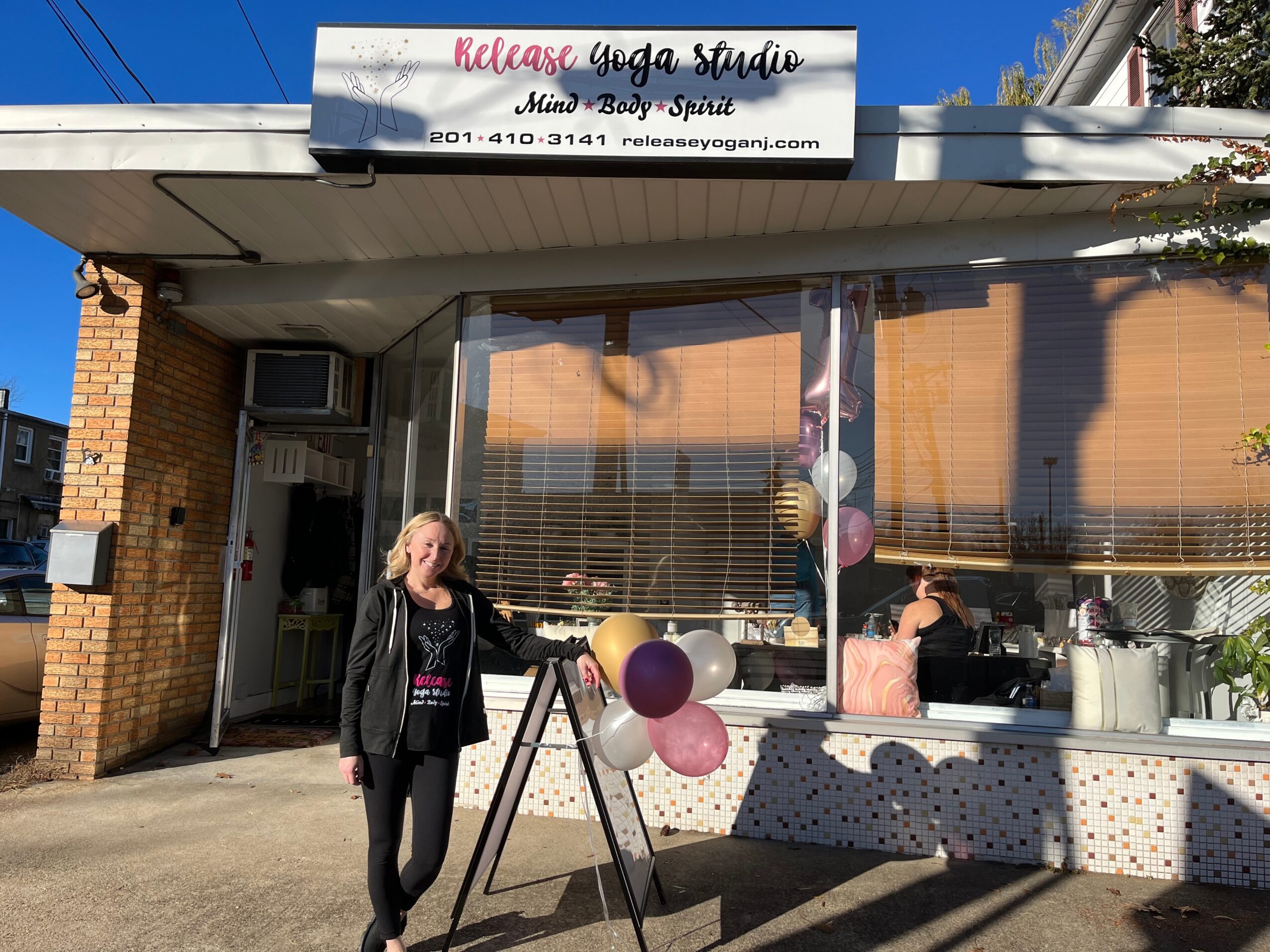 Front view of a yoga studio with large window, balloons outside, and a person standing near the entrance.