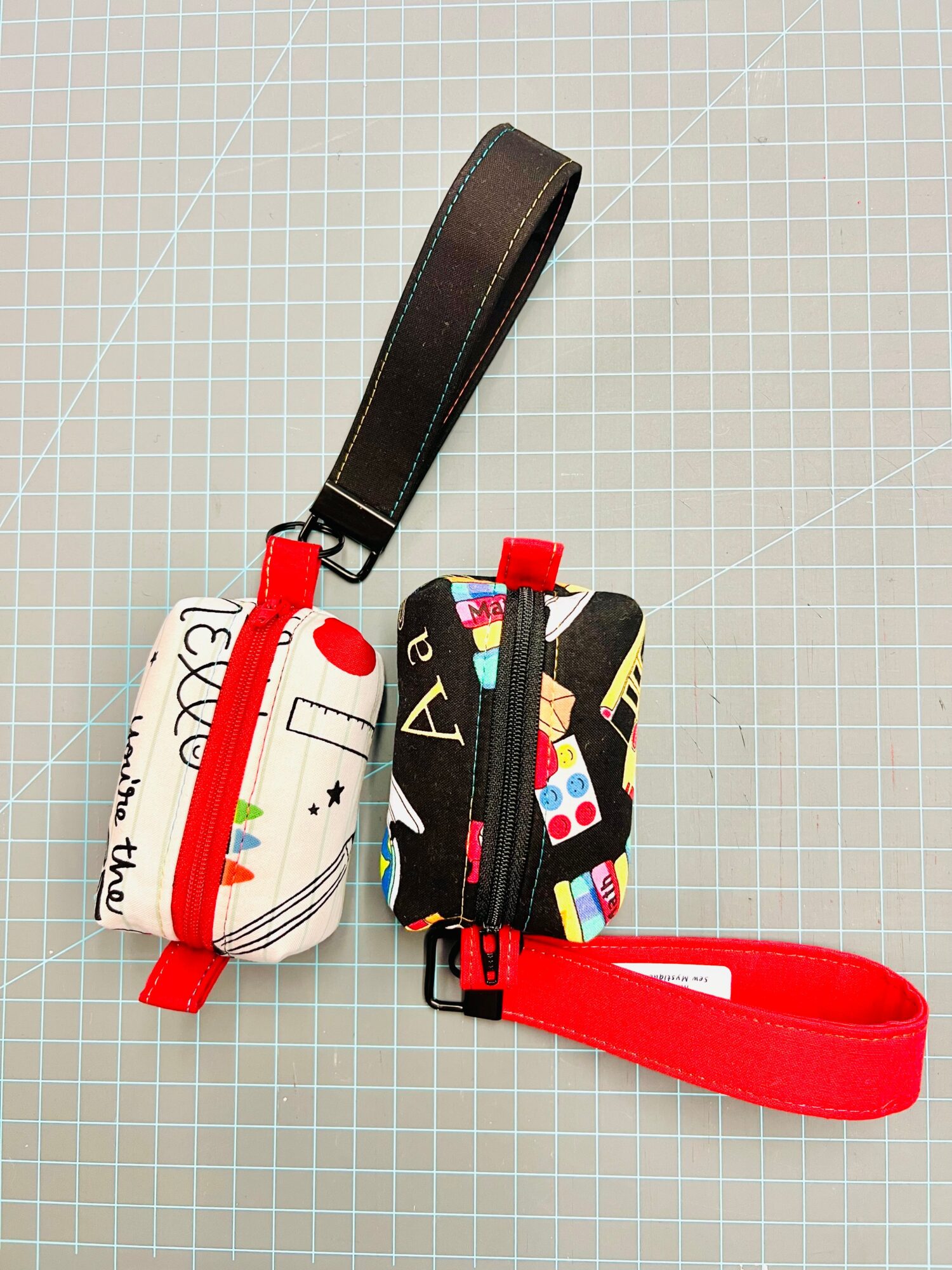 Two small pouches with straps, one with colorful patterns and the other with a white background and red accents, on a grid surface.