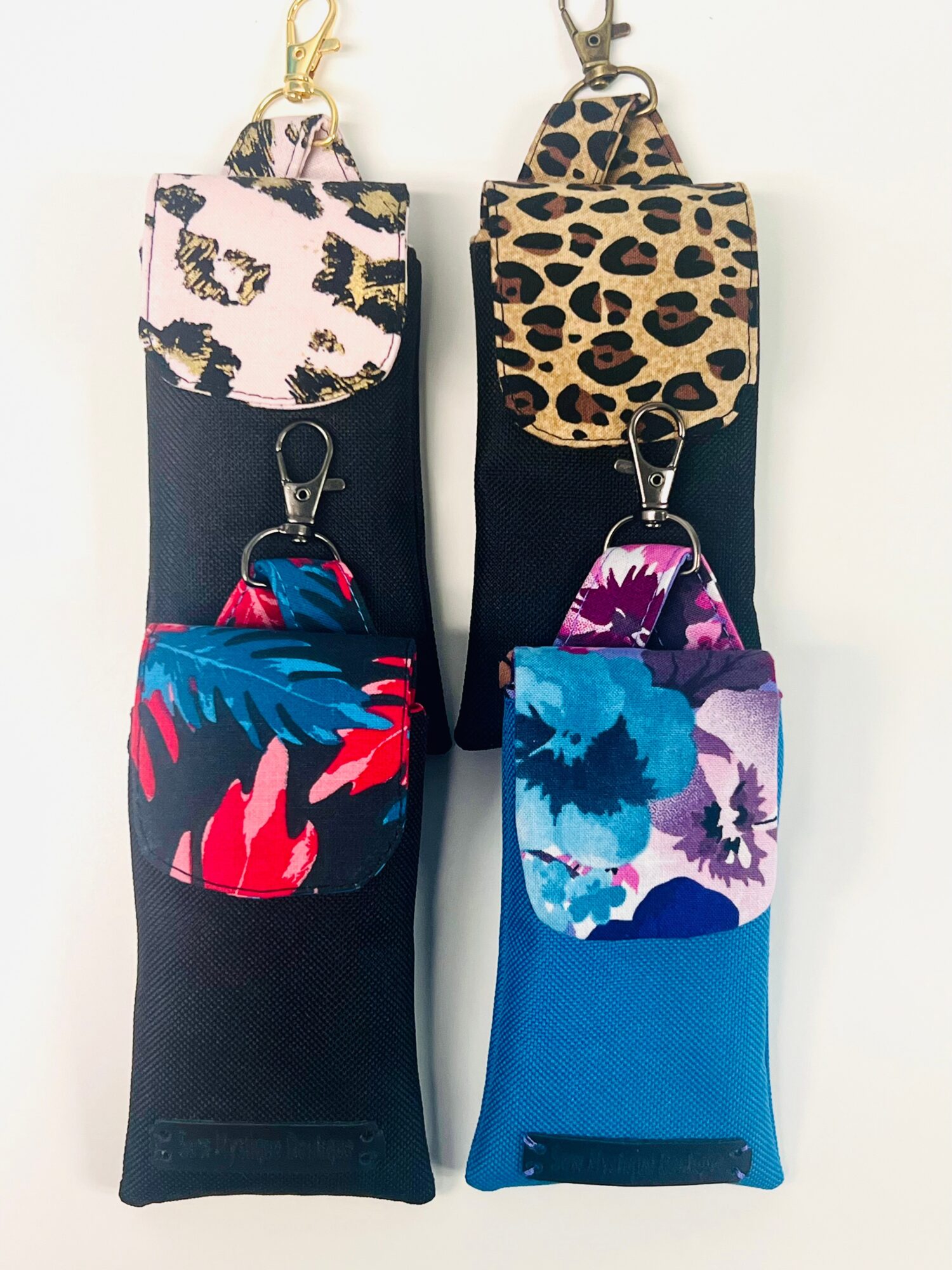 Four small pouches with colorful floral and animal print designs, attached to black straps, displayed vertically.