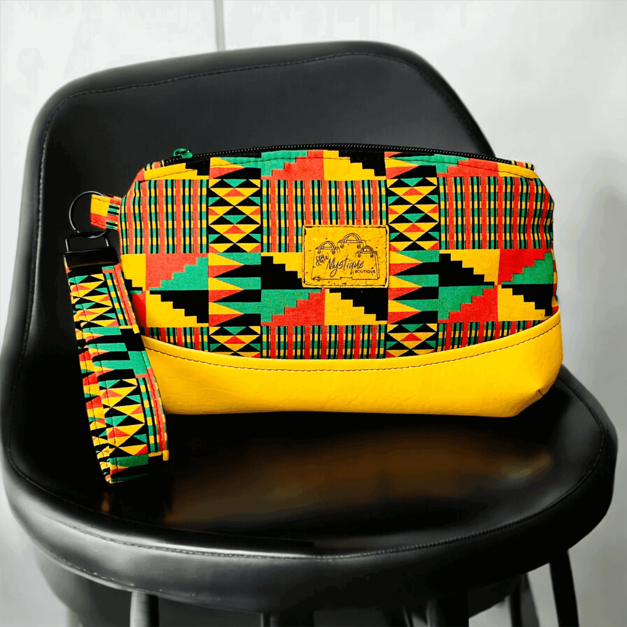 Colorful patterned bag with yellow bottom on a black chair, fabric strap attached, against a plain background.