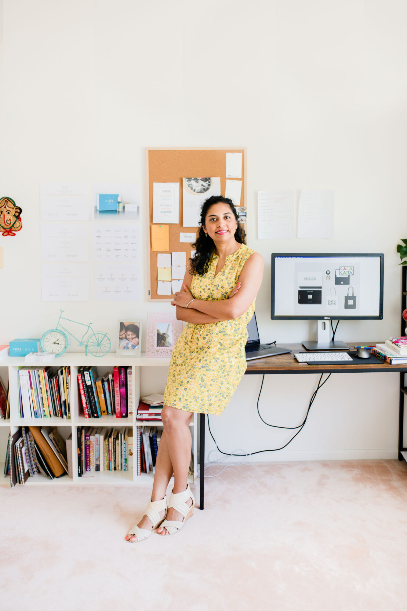 Woman in yellow dress standing in an office with bookshelves, computer, and bulletin board behind her.