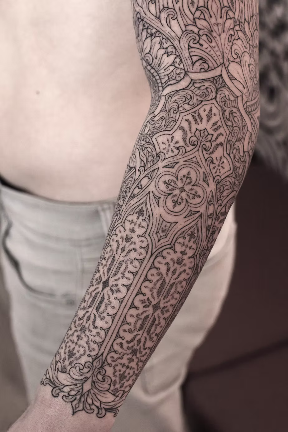 Arm with detailed black tattoo extending from wrist to elbow, featuring floral and geometric patterns.