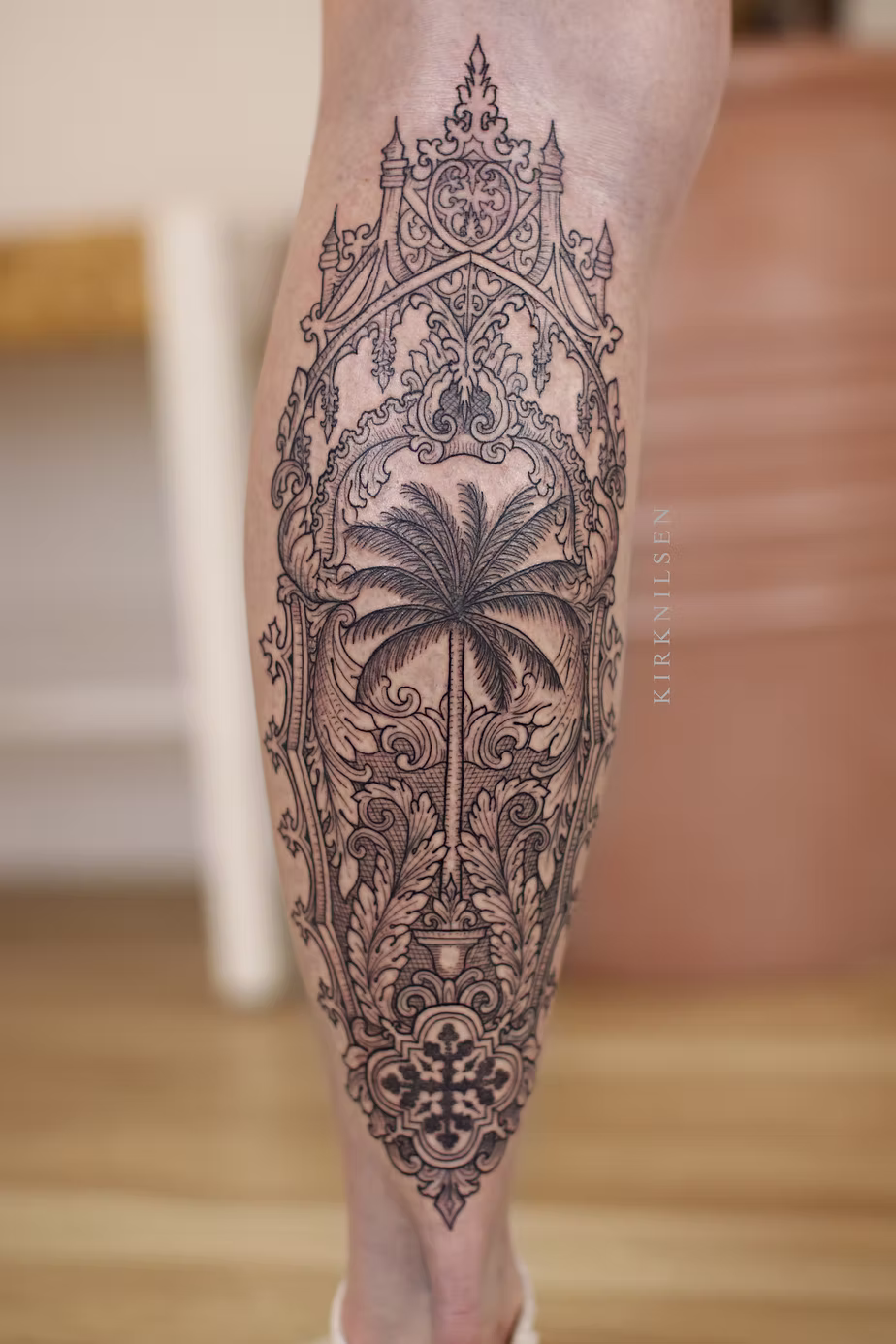 Intricate tattoo with floral and ornamental patterns on a person's lower leg, featuring a central flower motif.