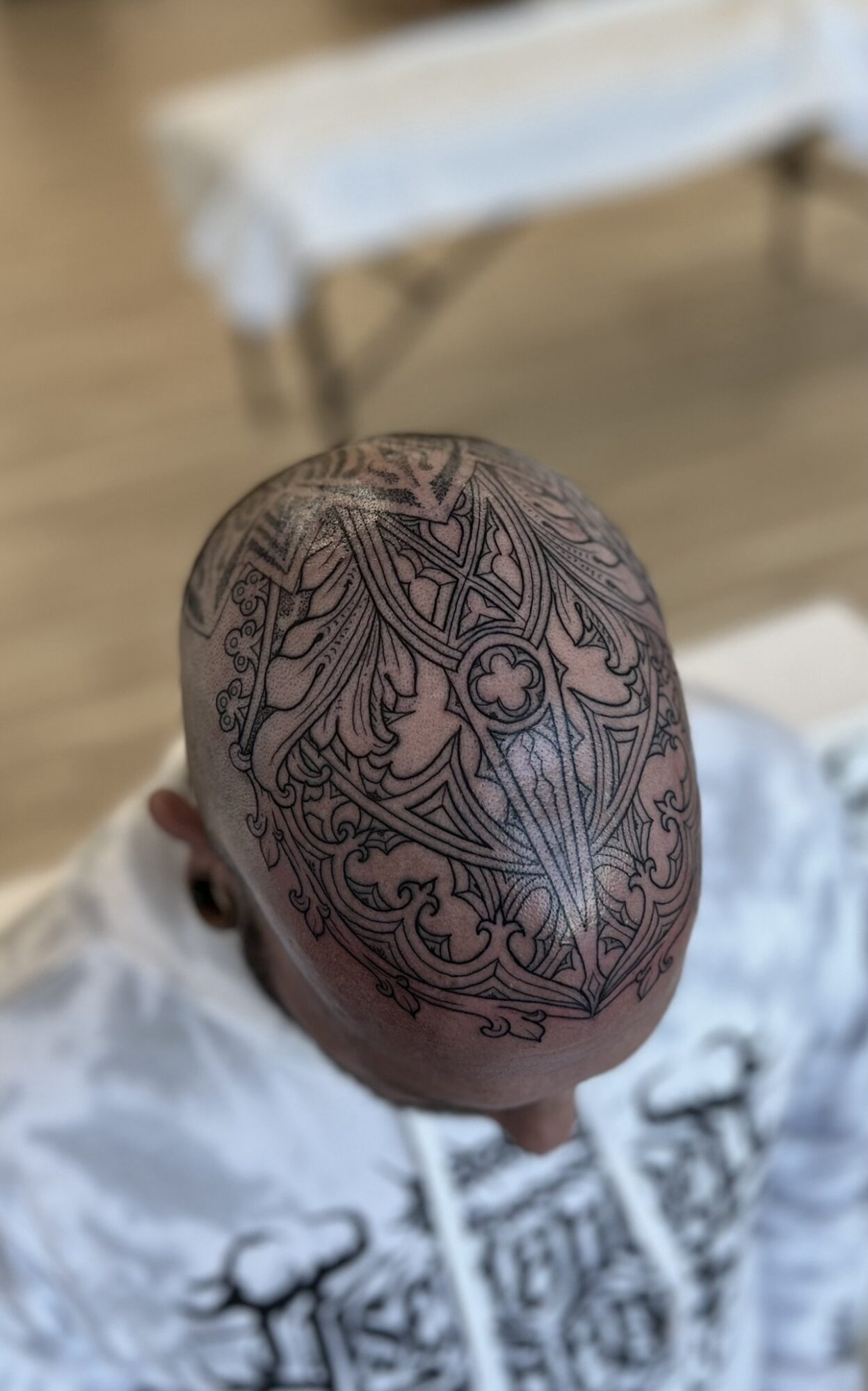 Top view of a person's head with intricate black tattoo designs covering the scalp, with a blurred background.