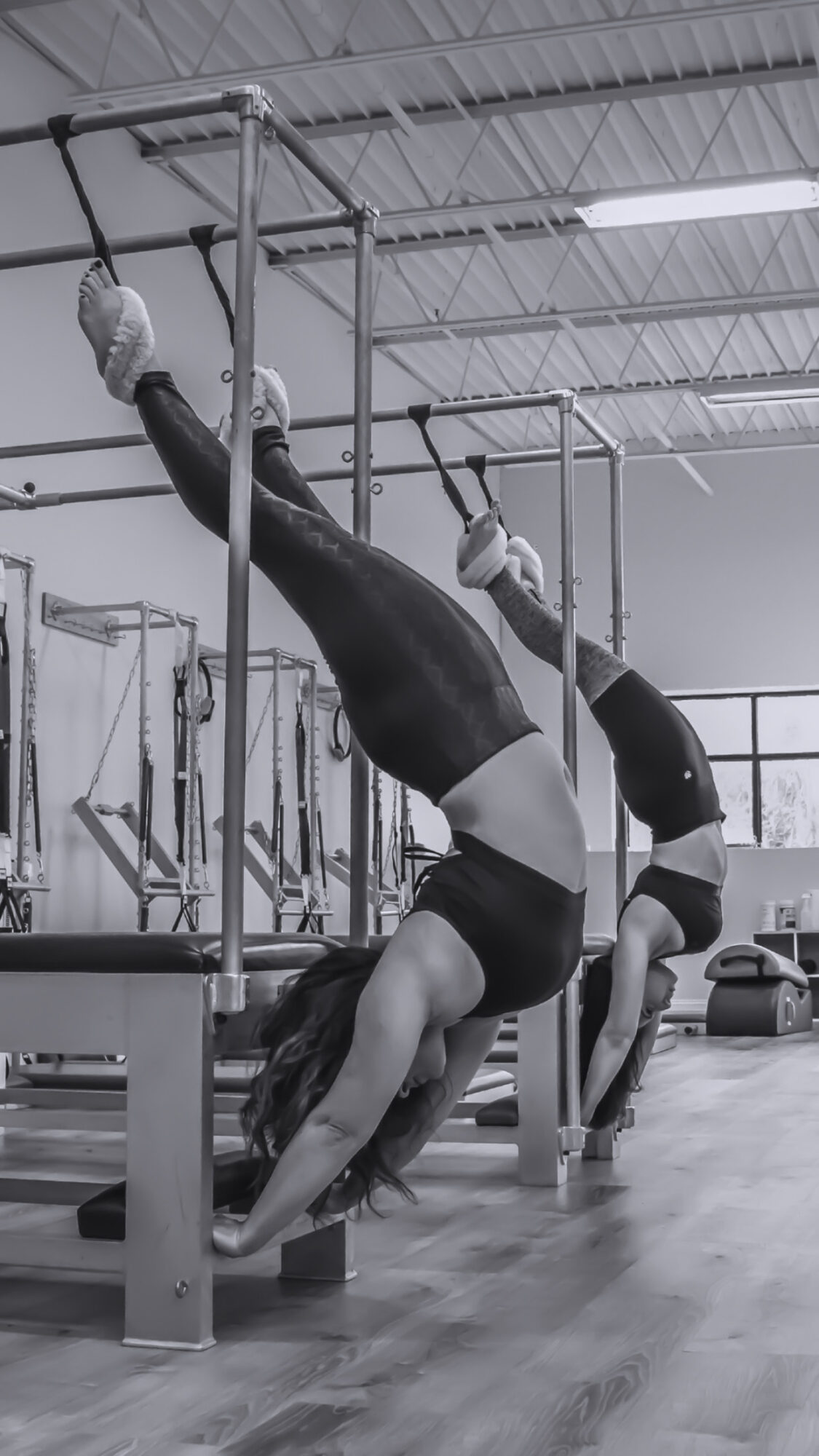Two women perform handstands on parallel bars in a gym, with one woman upside down and the other in a handstand position.