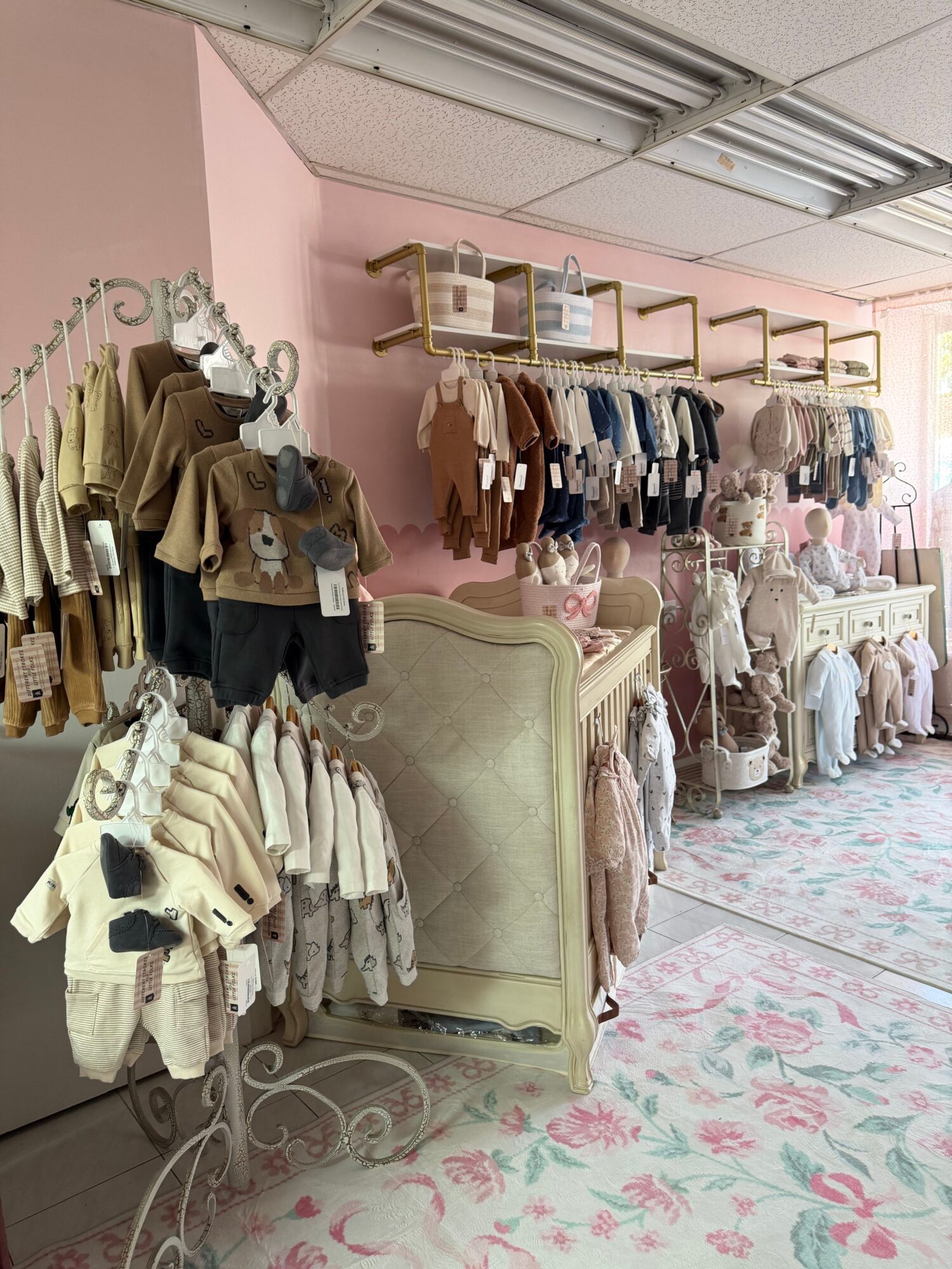 Clothing store with racks of clothes, shelves, and a vintage sofa, decorated with pink walls and floral carpet.