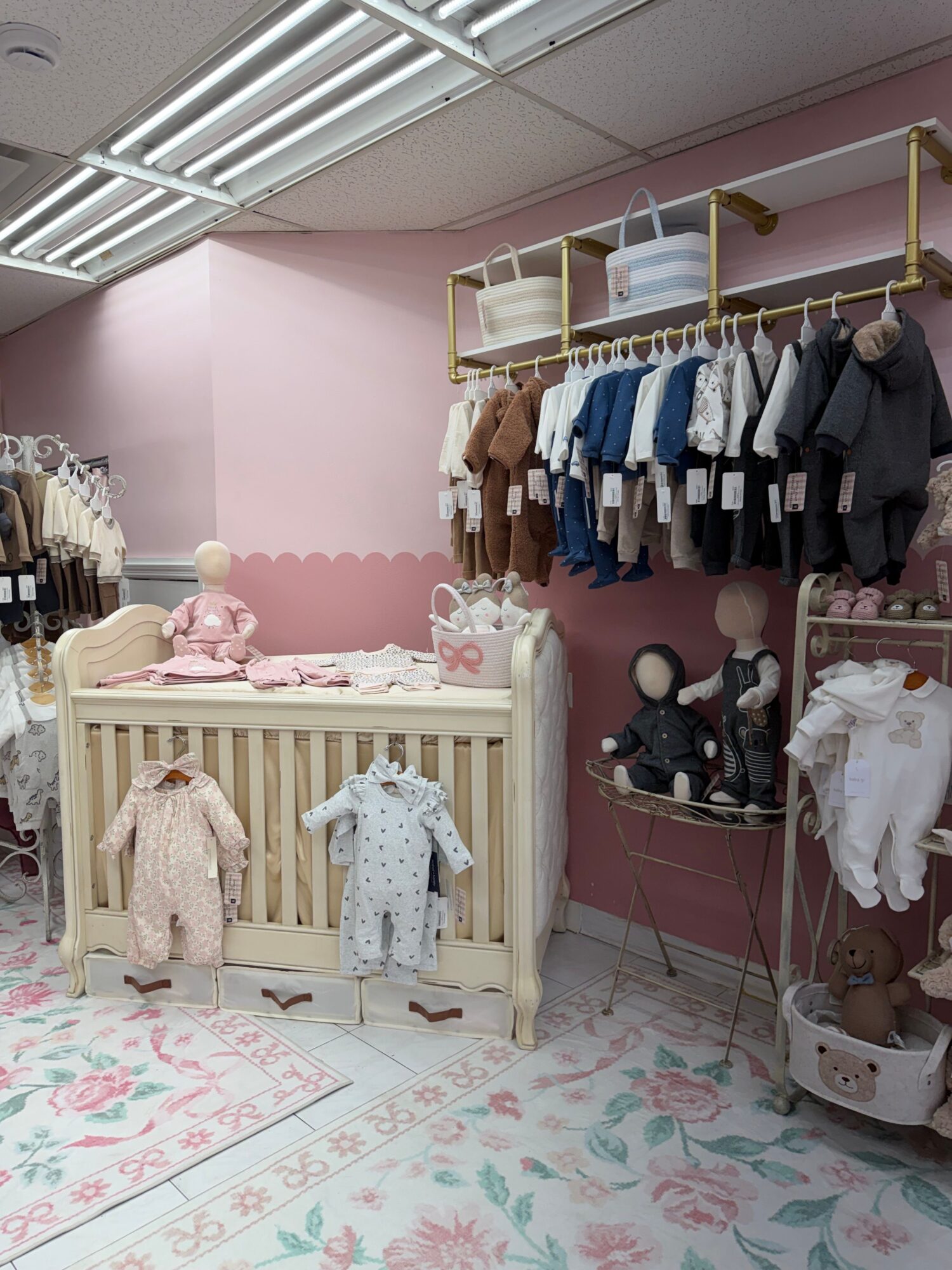 Children's clothing display with dresses on a wooden bed and racks of clothes in a pink-themed store.