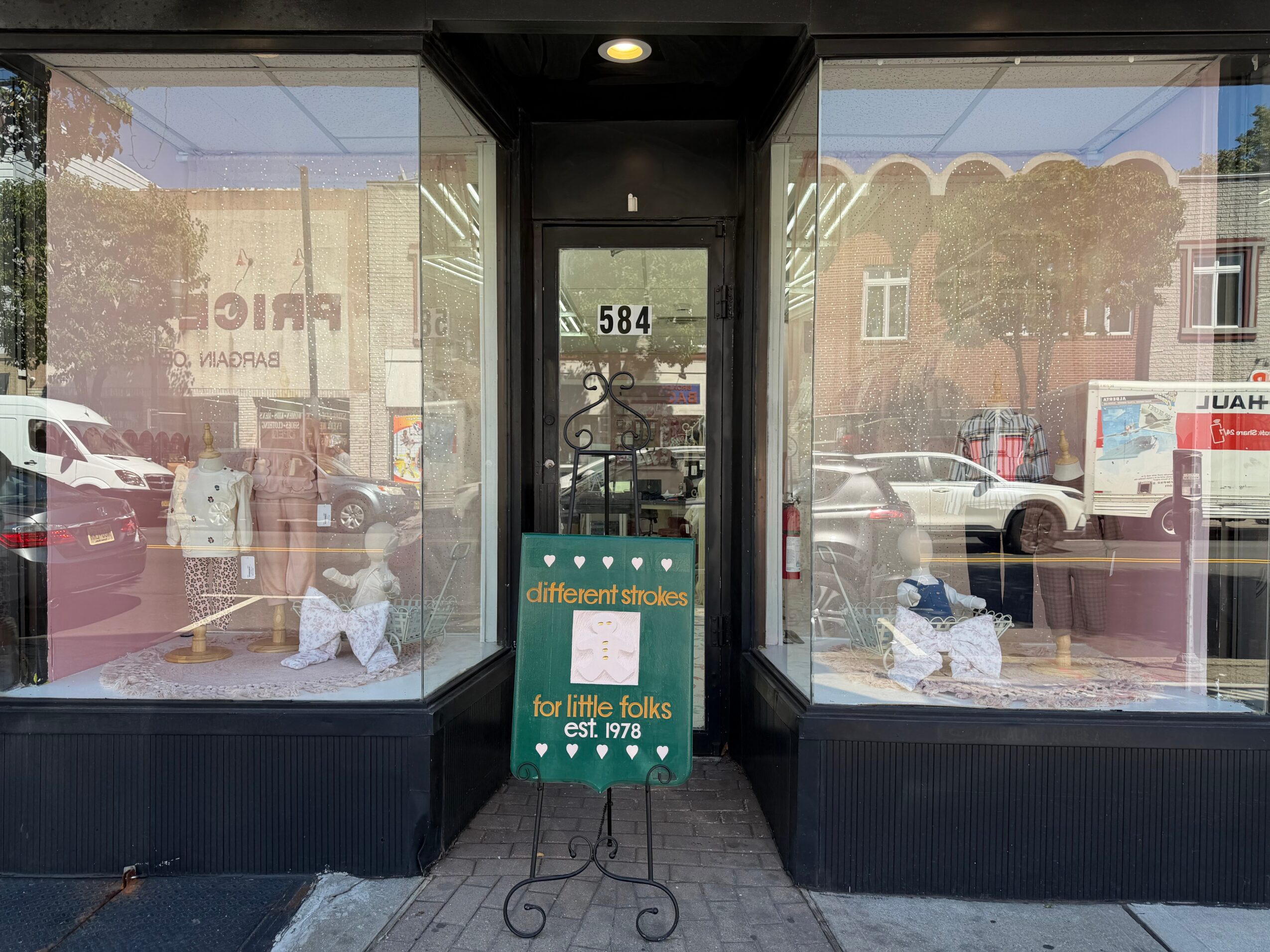 Storefront with large glass windows and a door in the center, reflecting parked cars and buildings outside.