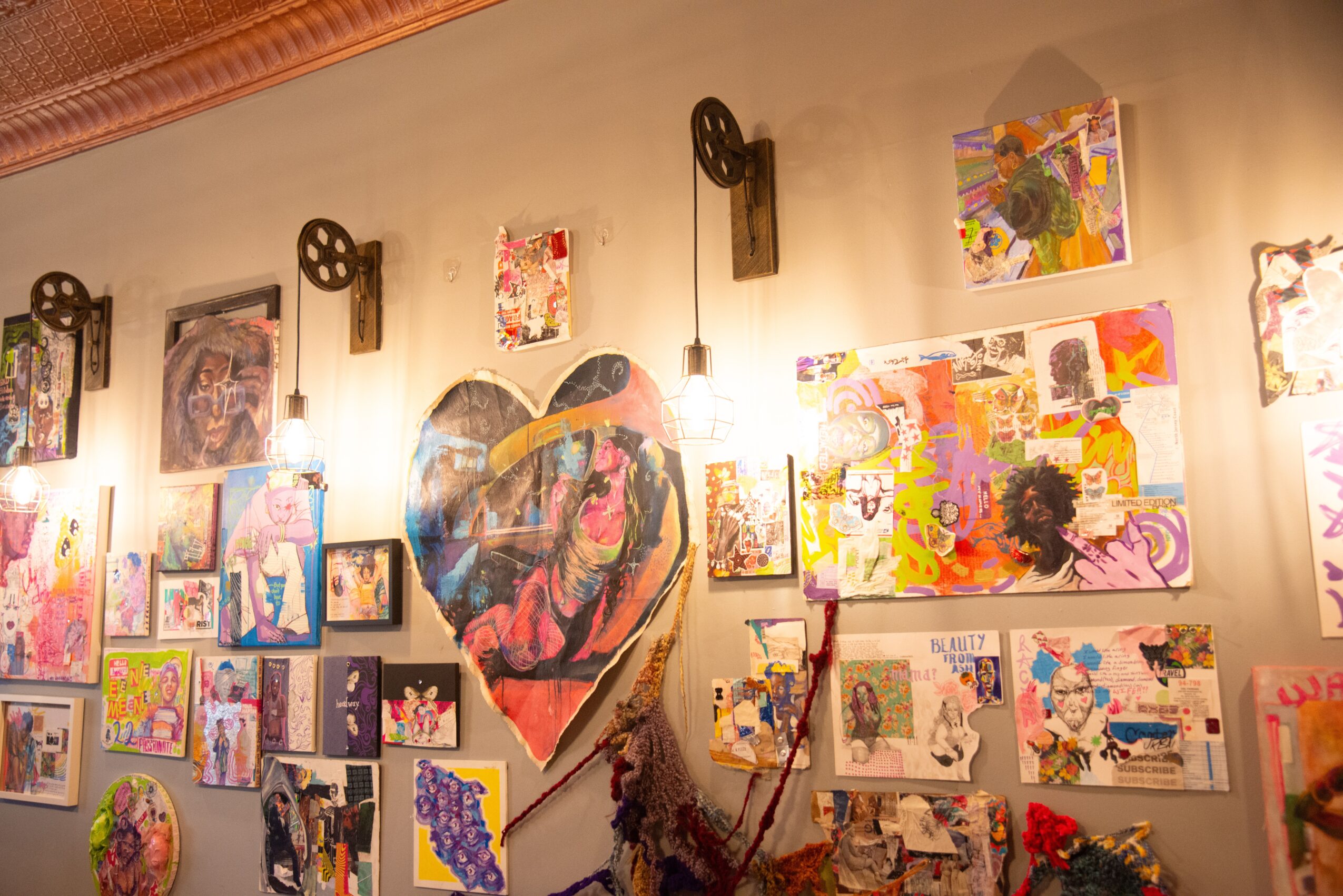 Gallery wall with colorful artwork, a large heart-shaped piece, and vintage film reels, illuminated by warm lighting.