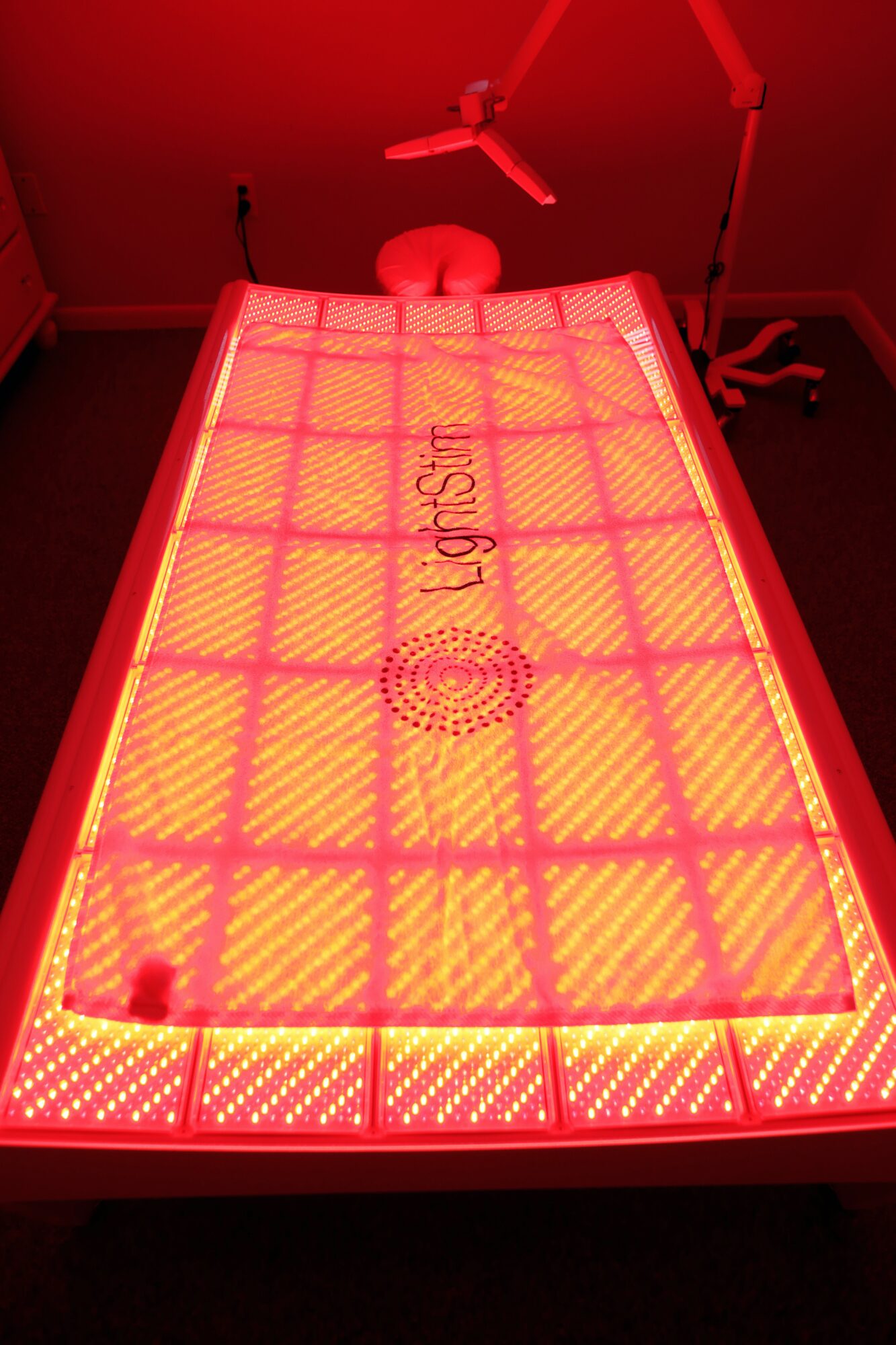 Red light therapy bed with grid pattern, in a room with red lighting, and a small stool nearby.