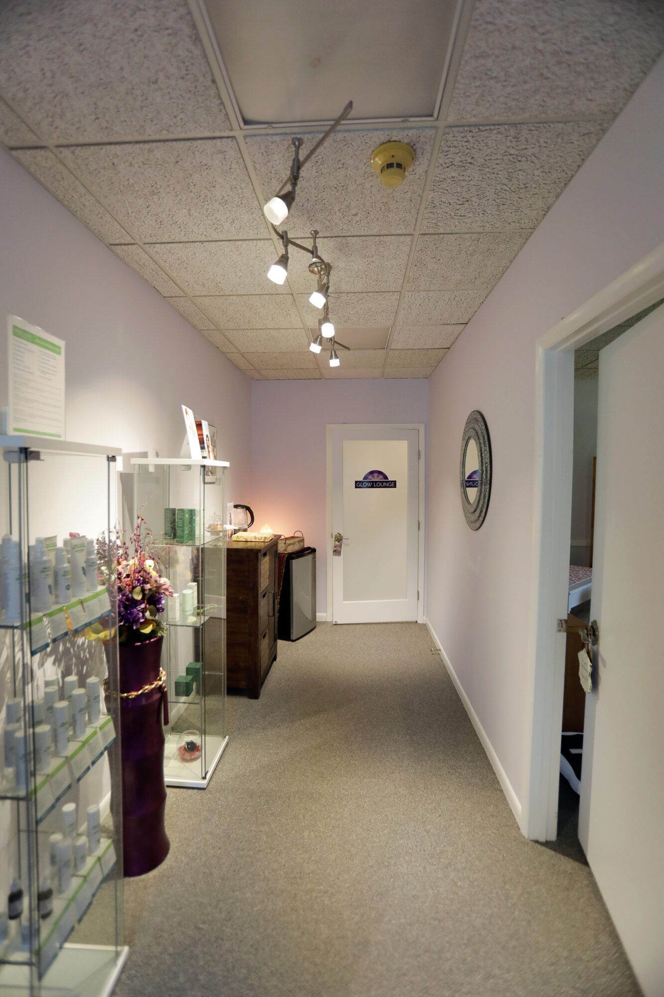 Hallway with display cases, a door at the end, and a round mirror on the right wall.
