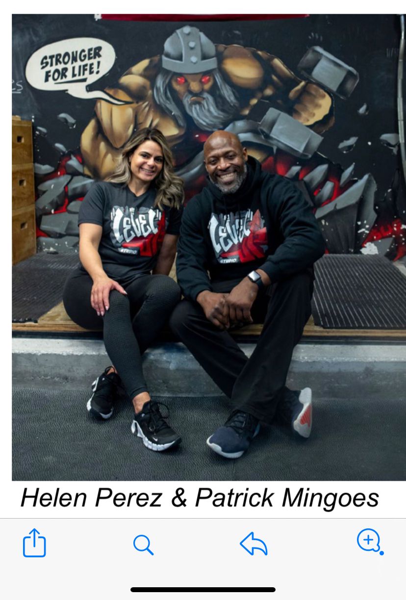 Two people sitting in front of a colorful mural, smiling, with a cartoon character in the background. Helen Perez and Patrick Mingoes.