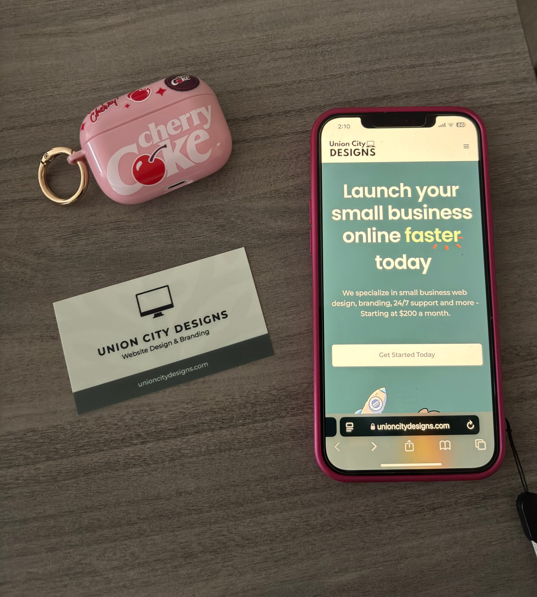 Pink cherry-flavored candy case, business card for Union City Designs, and a smartphone displaying a business promotion webpage on a gray surface.