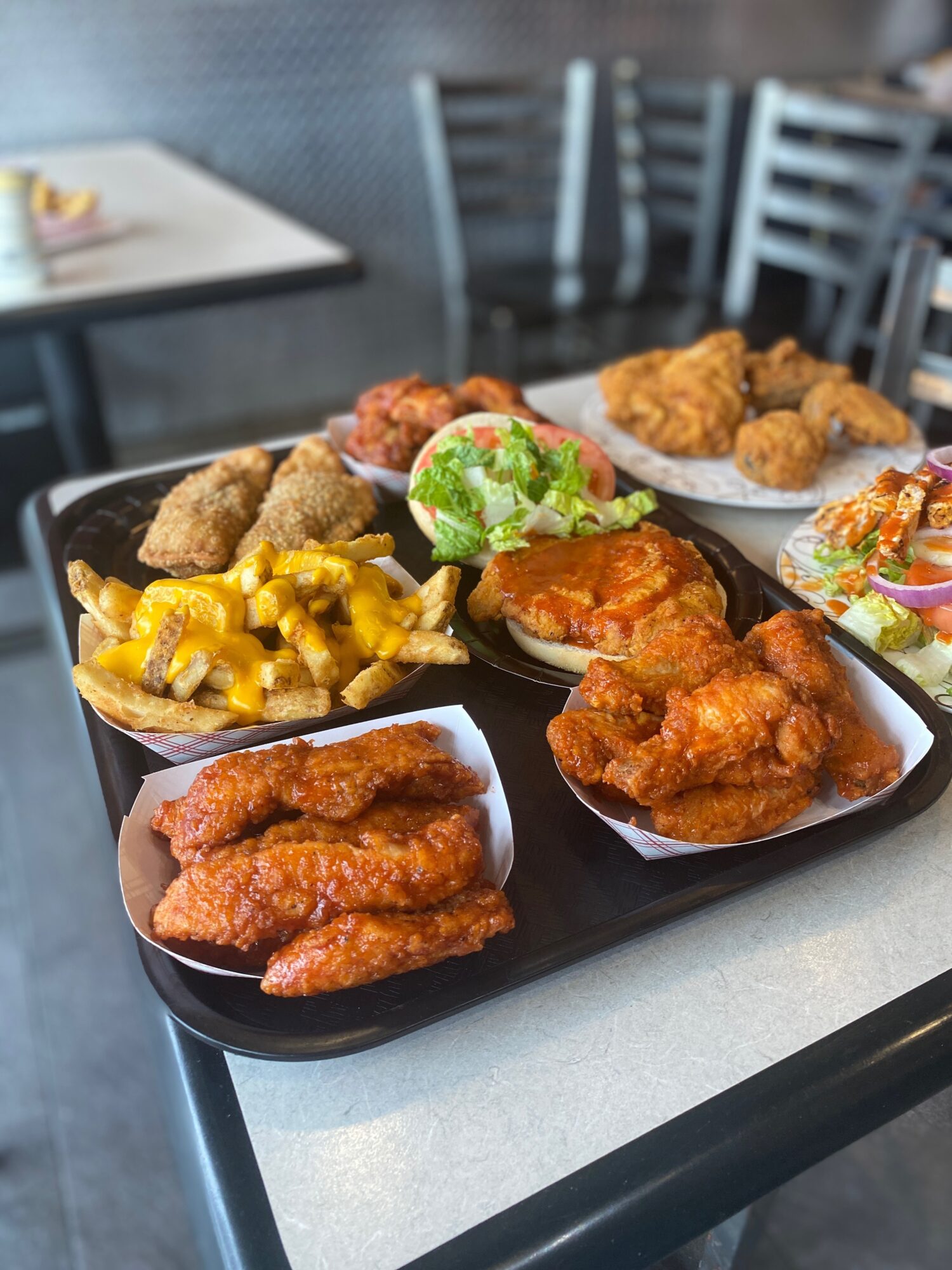 Assorted fried chicken and side dishes on black and white plates on a table, with chairs in the background.