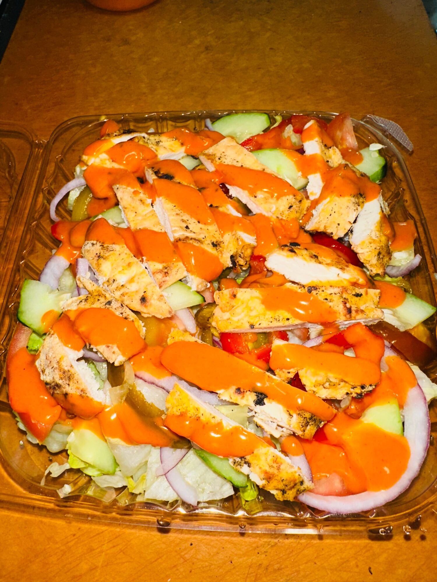 Salad with sliced bread, orange sauce, cucumber, and onion in a glass dish on a wooden surface.