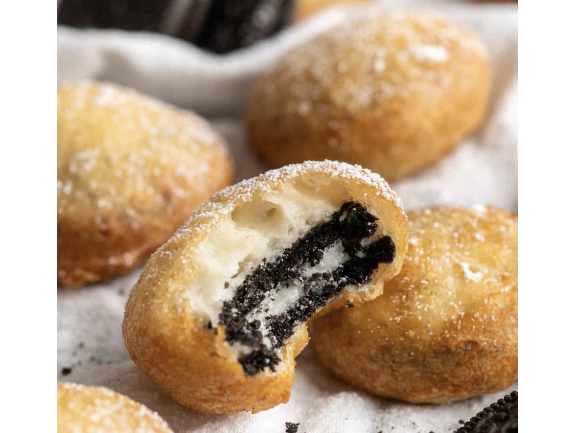 Fried doughnuts with powdered sugar, one cut open revealing black filling, on a white surface.
