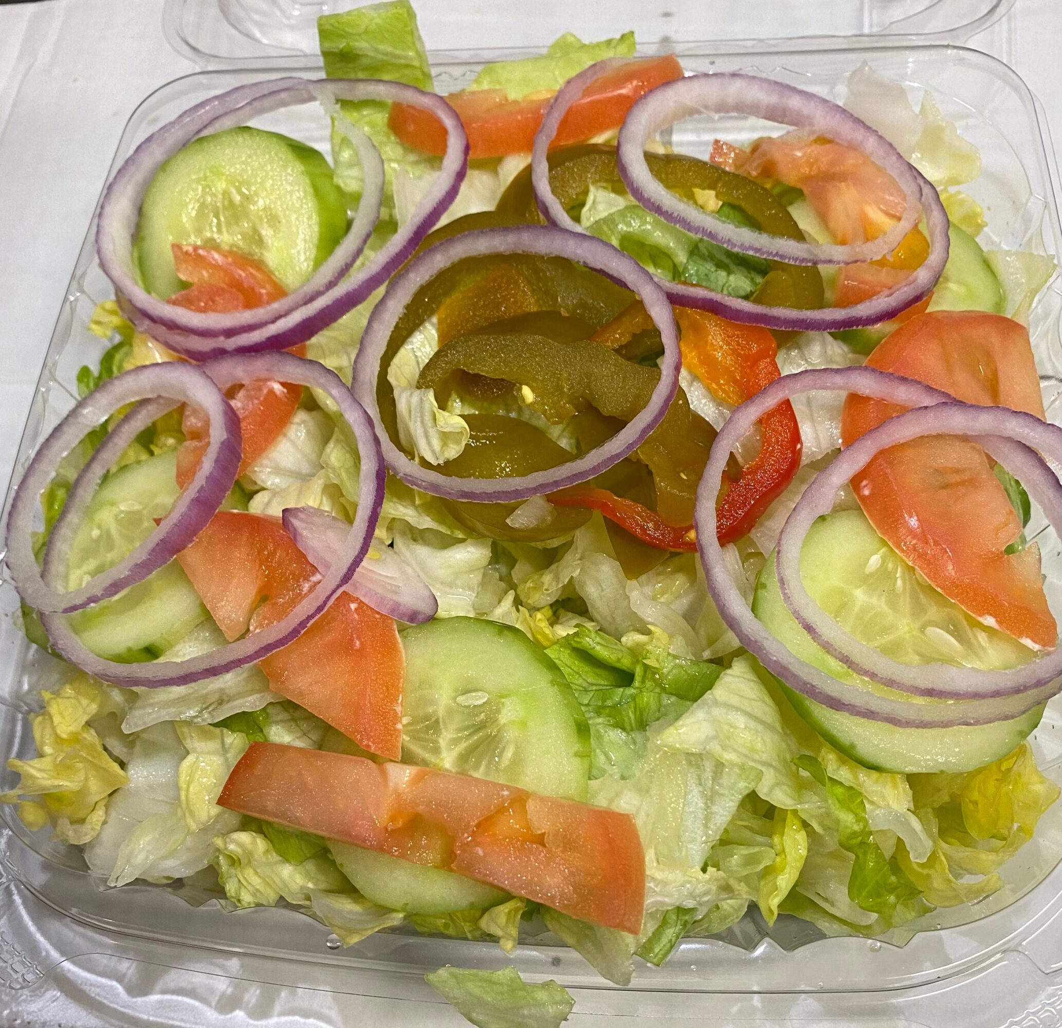 Fresh salad with lettuce, cucumber, tomato, red onion, and green pepper slices in a clear container.