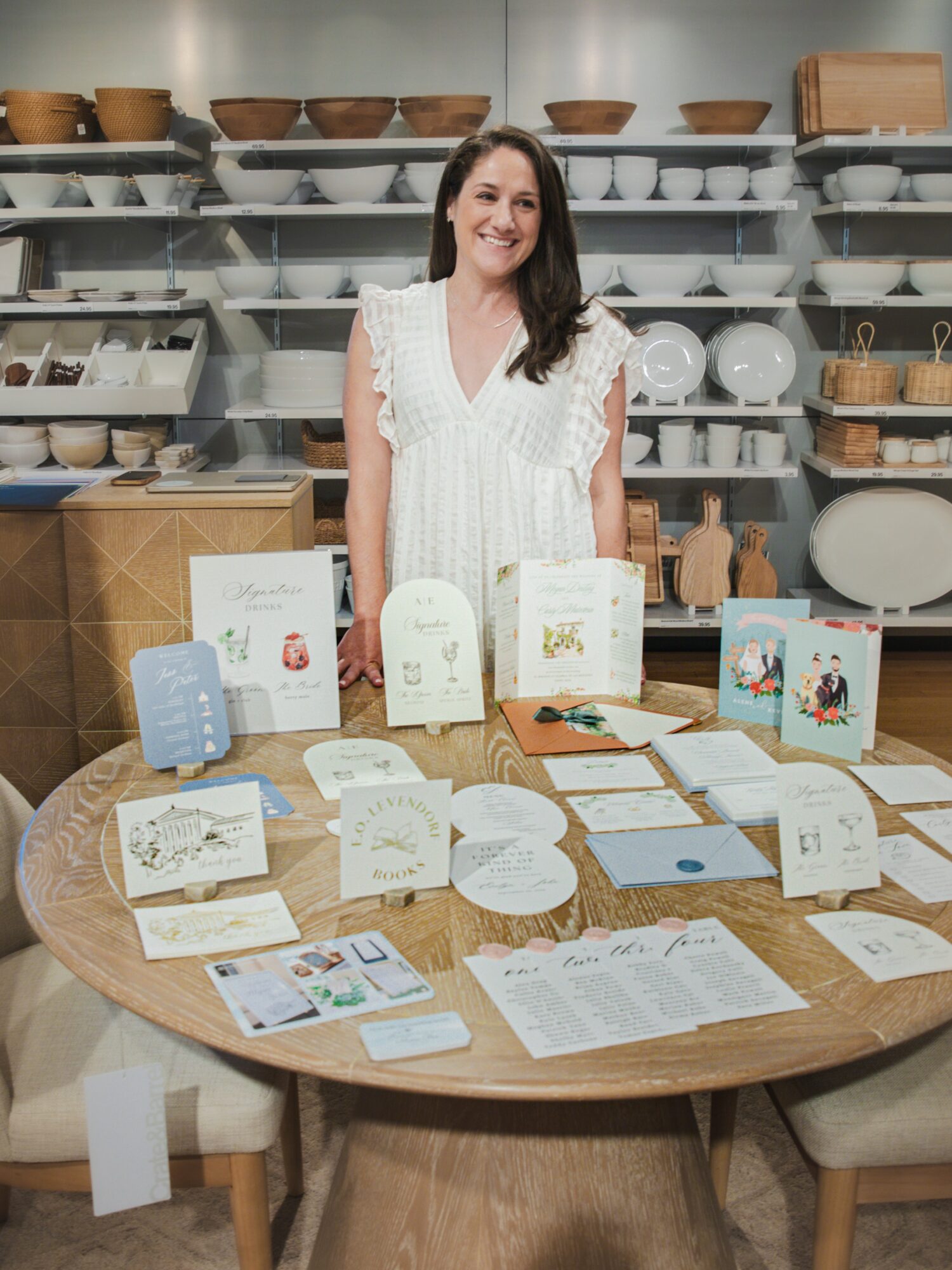 Woman standing behind a table with various packaged products in a store or workshop setting.