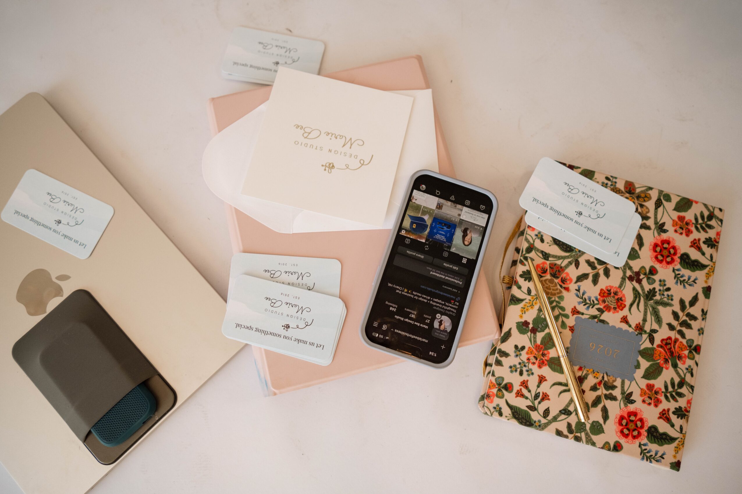 Flat lay of a laptop, sticky notes, a smartphone, and a floral notebook on a light surface.