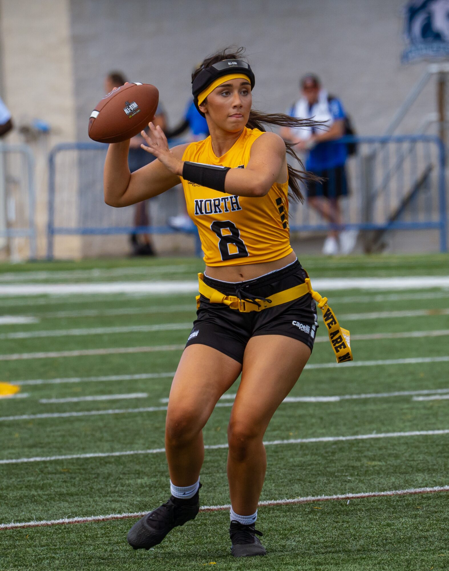 Female football player in yellow and black uniform prepares to throw a football on field.