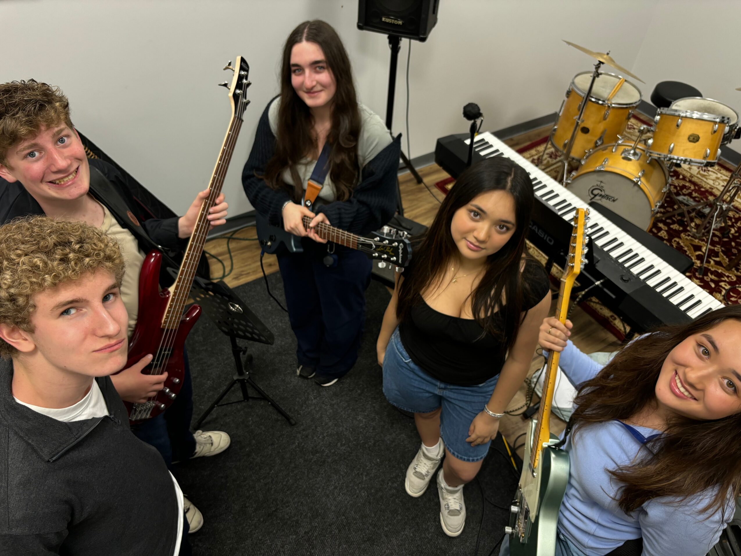 Group of five young people with musical instruments in a room, smiling and posing for the photo.