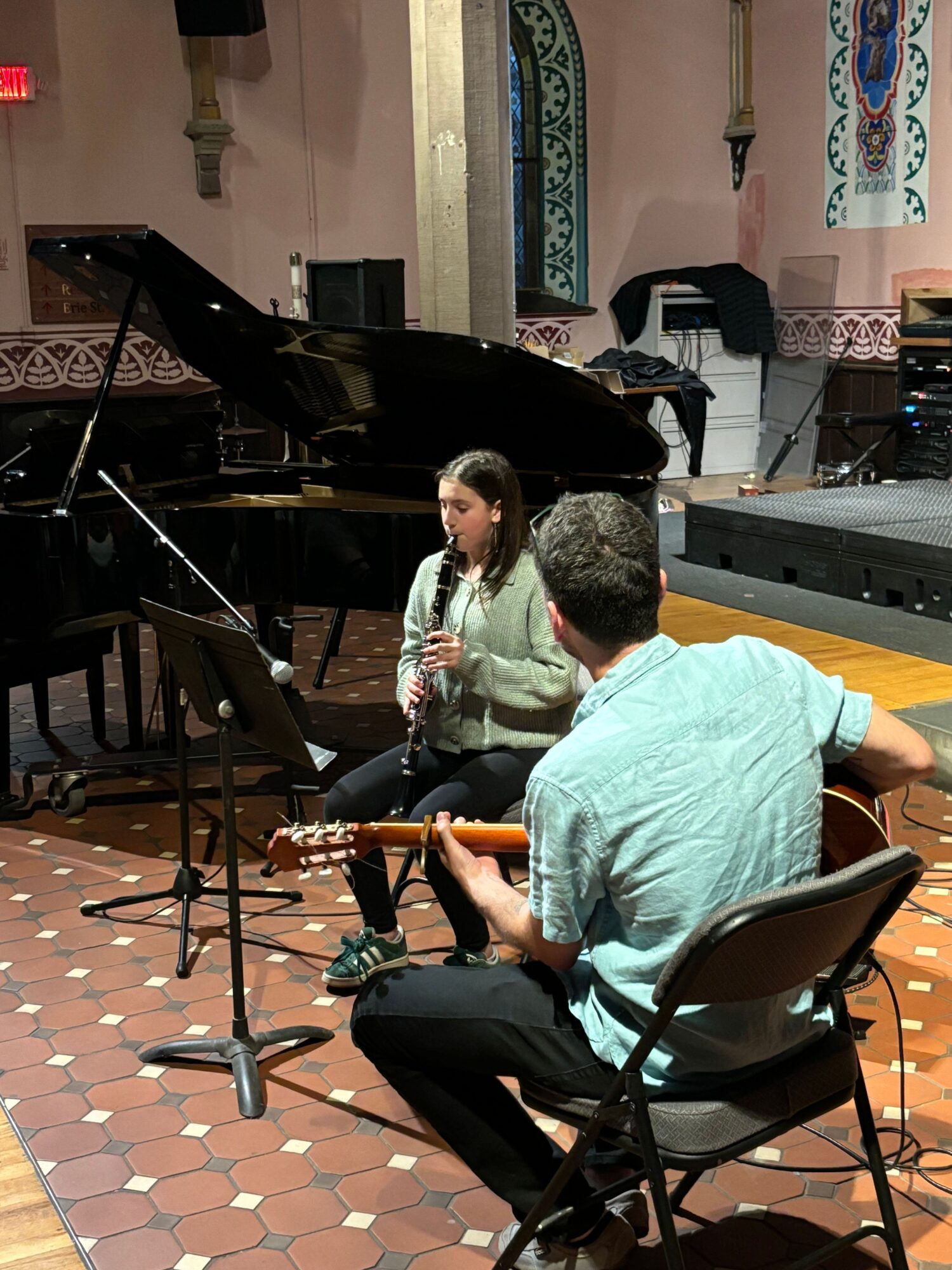 Two musicians perform with a grand piano in a decorated room, one playing the piano and the other singing into a microphone.