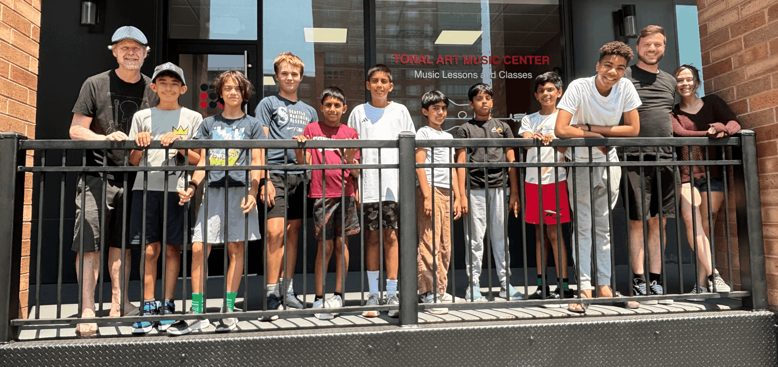 Group of children and adults standing on a balcony railing outside a building, smiling and posing for the photo.