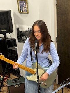 Woman with long brown hair holding a yellow electric guitar and standing in a room with musical equipment.