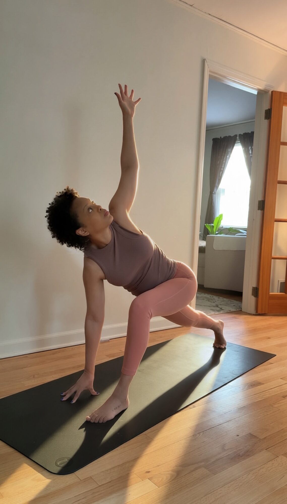Person practicing yoga in a room, balancing on one hand and foot with the other arm raised, on a black mat.